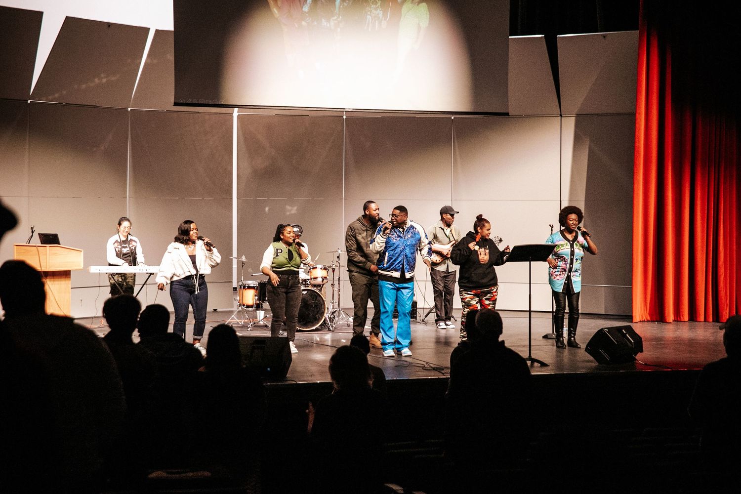 Audience members standing and engaging with a performance in a darkened auditorium.
