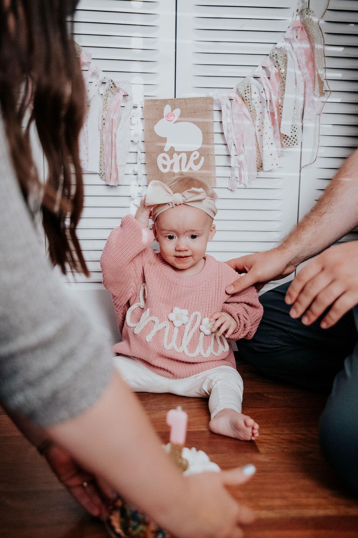 Small baby wearing pink during first birthday cake smash photoshoot with white frosted cake.