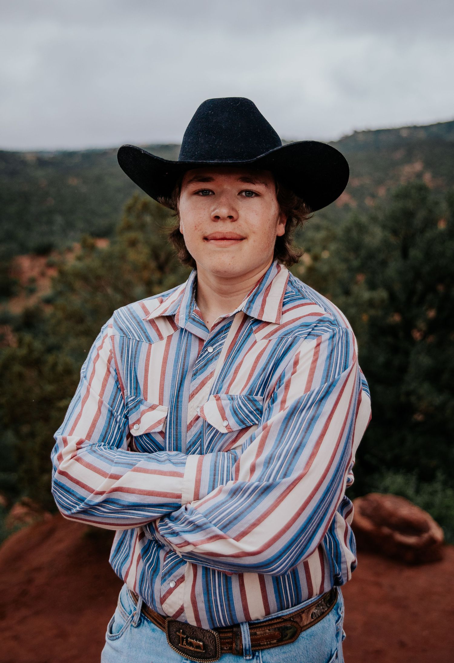 A high school senior in cowboy attire stands on red rocks overlooking a mountain valley at Garden of the Gods in Colorado Springs