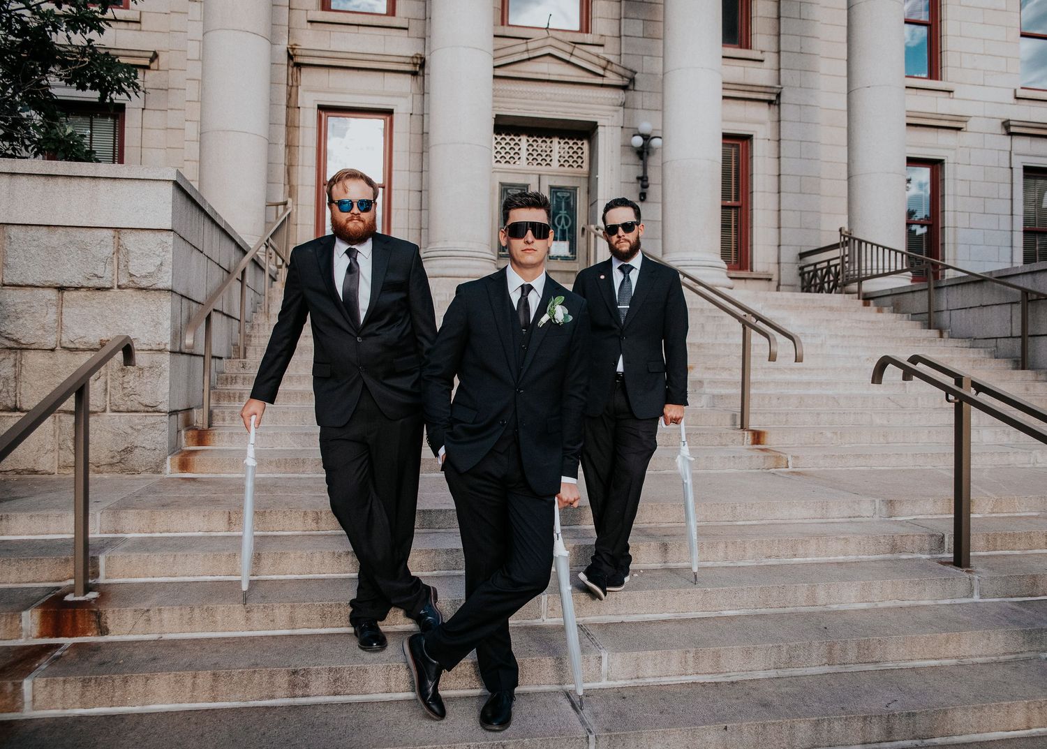 Wedding party members in formal attire descending stone steps of a classic building.