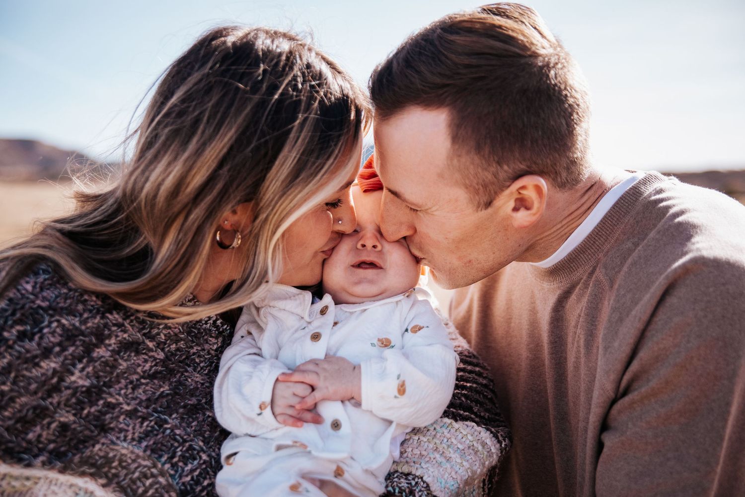 Family embracing in a tender moment against a sunlit desert landscape setting.