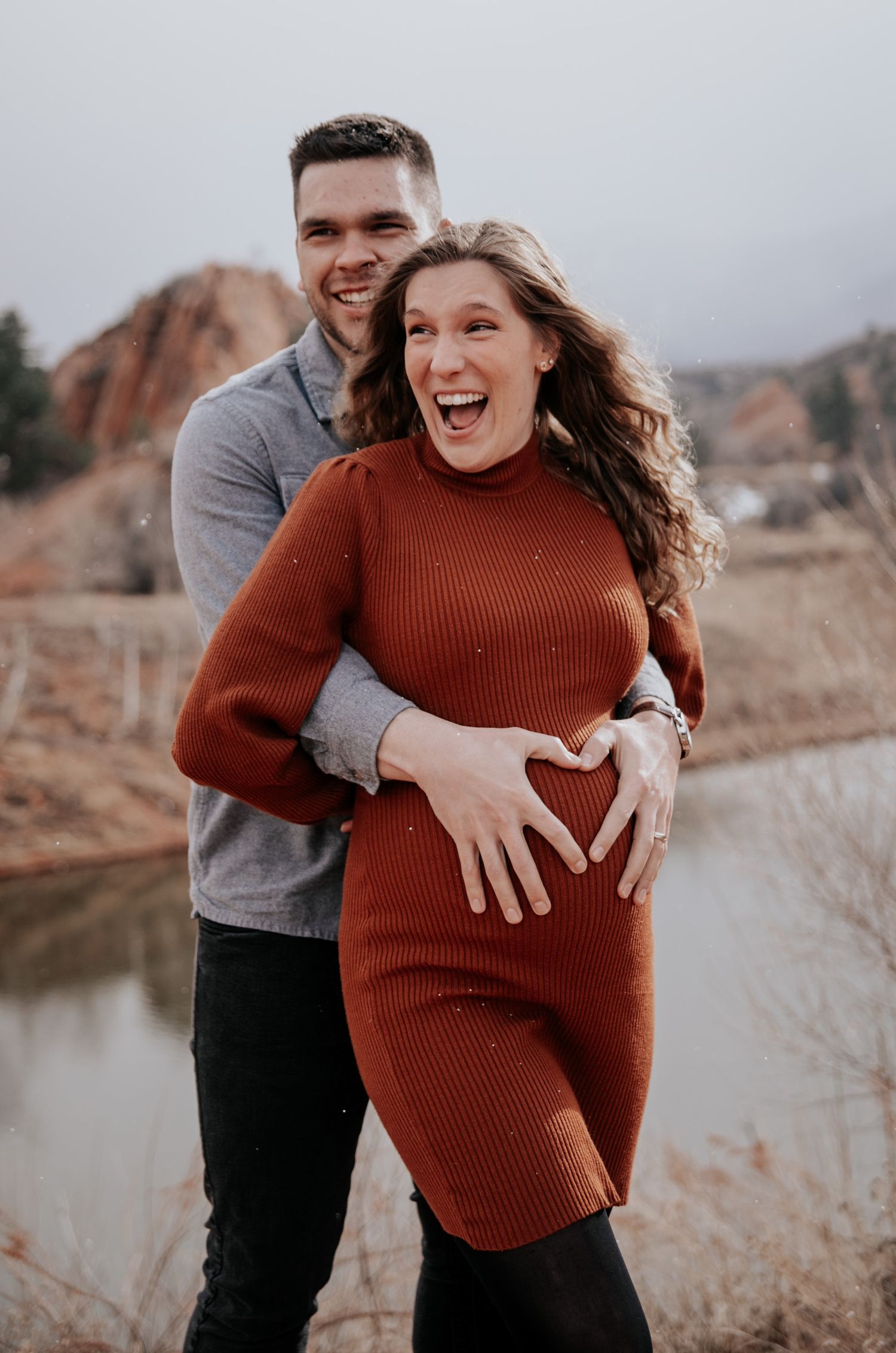 A joyful couple laughs together during their outdoor maternity session near red rocks.