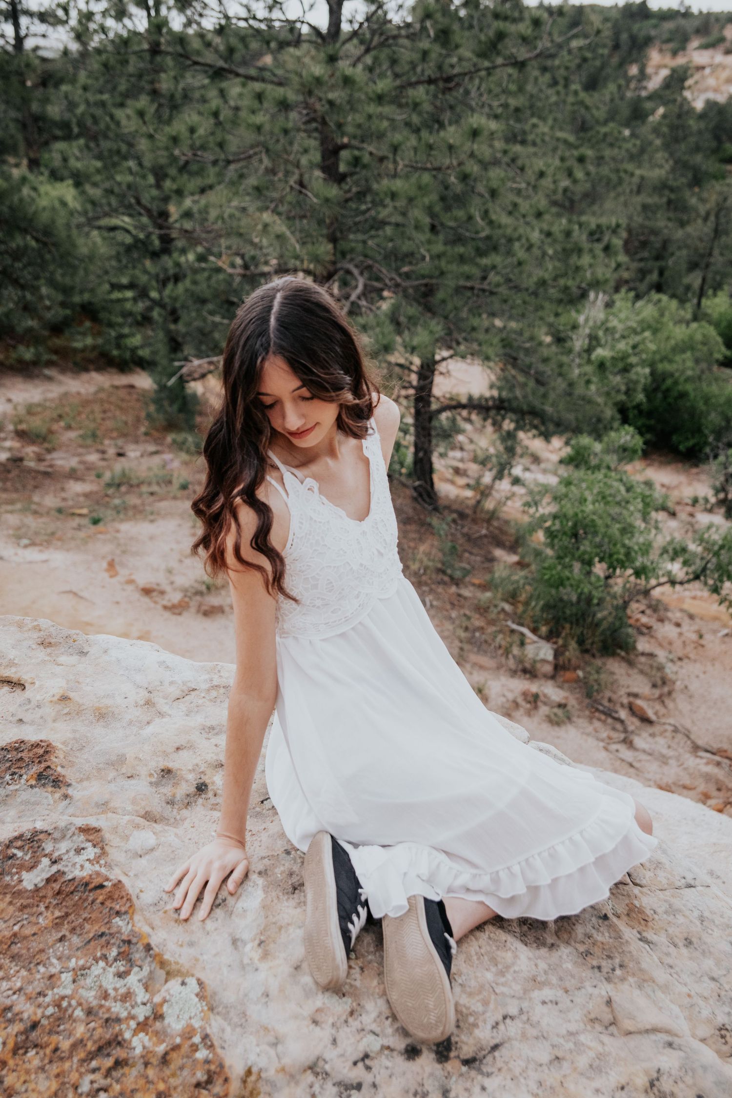 A person in a white dress exploring rocky terrain during a photo session.