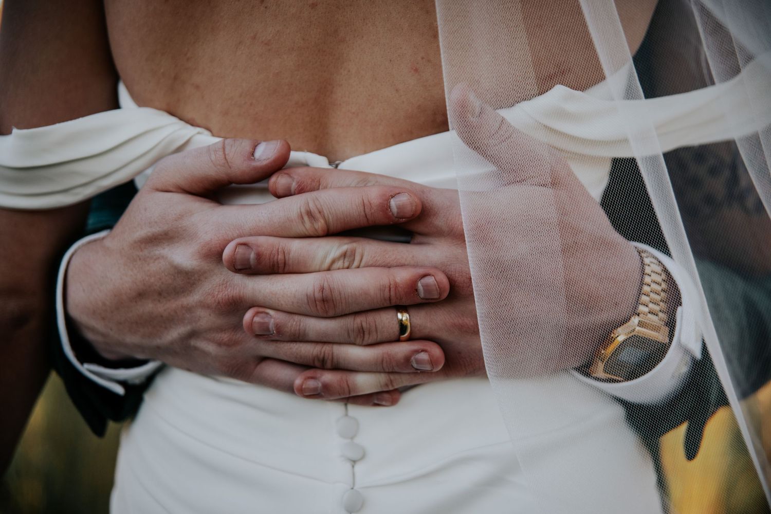 Intimate wedding moment captured with hands touching in soft natural lighting.