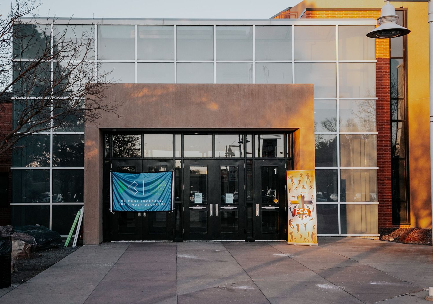 Modern building exterior with glass panels and a blue banner hanging above entrance doors.