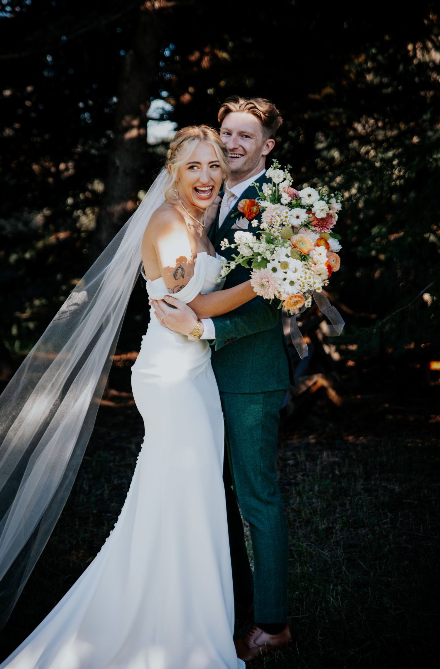 A joyful wedding portrait with a beautiful bouquet and flowing veil in natural outdoor lighting.