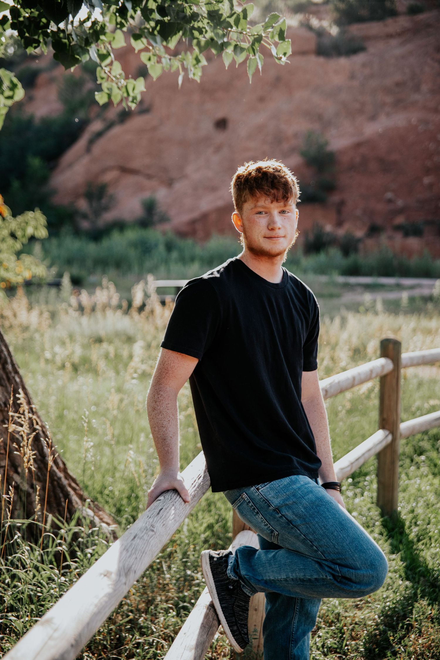 Guy leaning on fence at Red Rock Open Space in Colorado Springs during senior photo session