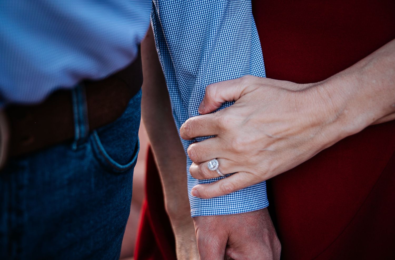 Close-up of hands and engagement ring against blue shirt and red dress.