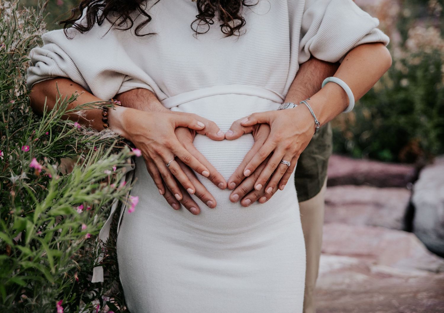 Multiple shots of hands cradling a pregnant belly in a white maternity dress.