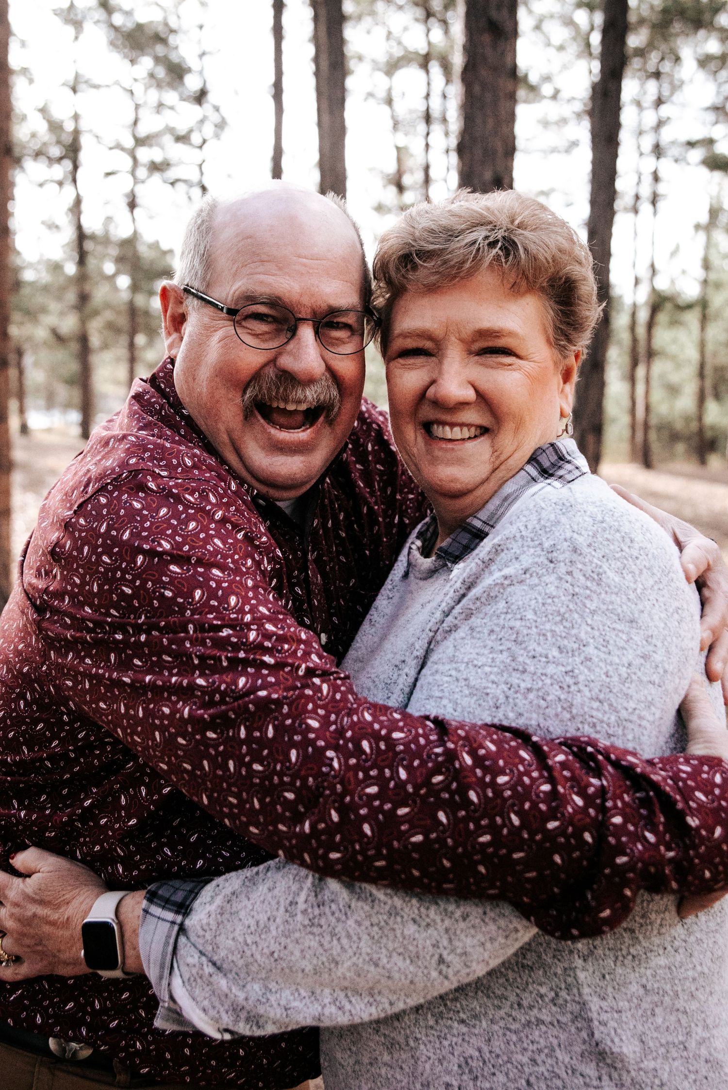 Loving embrace shared between couple wearing burgundy and gray in winter forest setting.