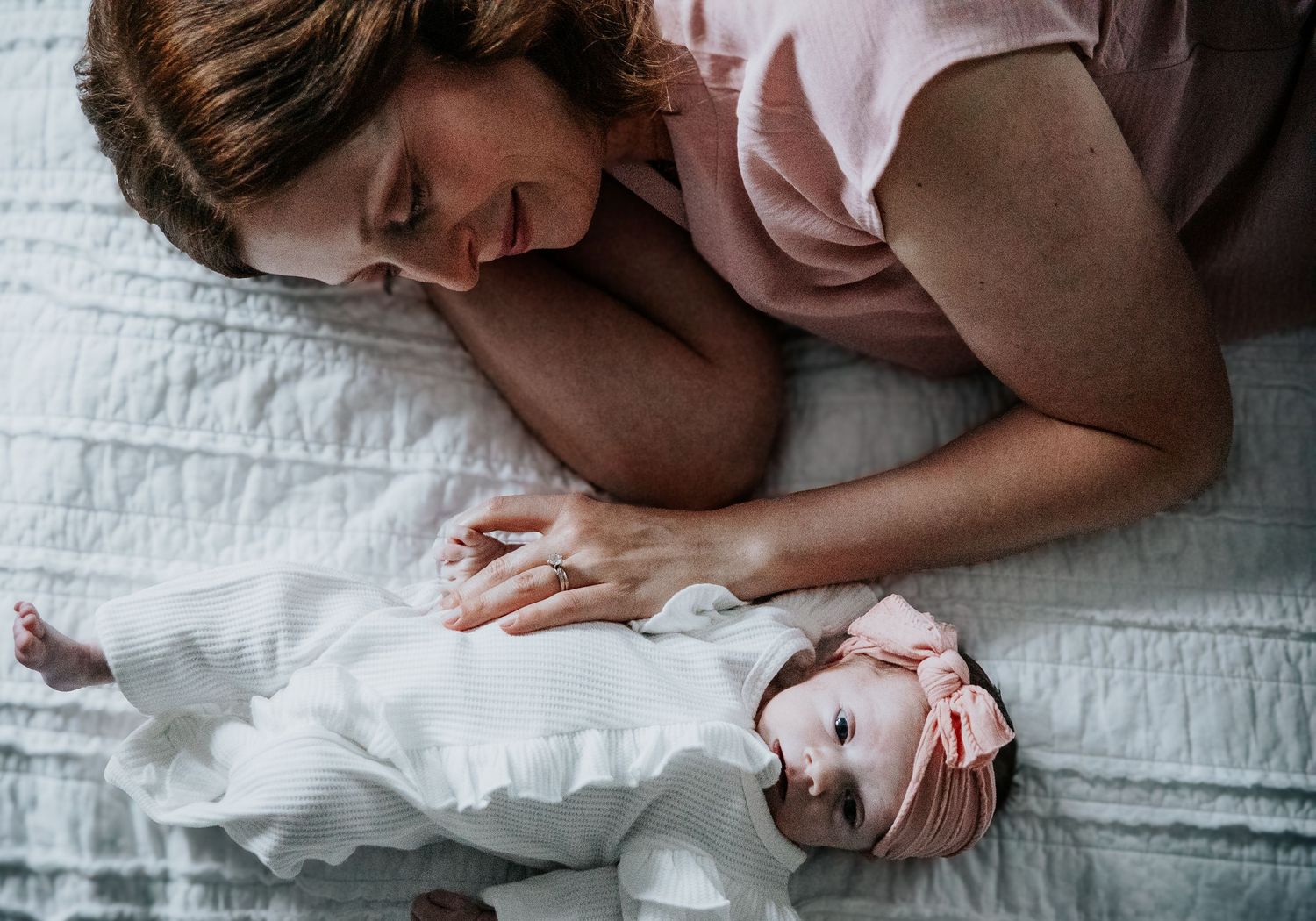 A sweet newborn photo session captures tender moments between parent and baby on white bedding.