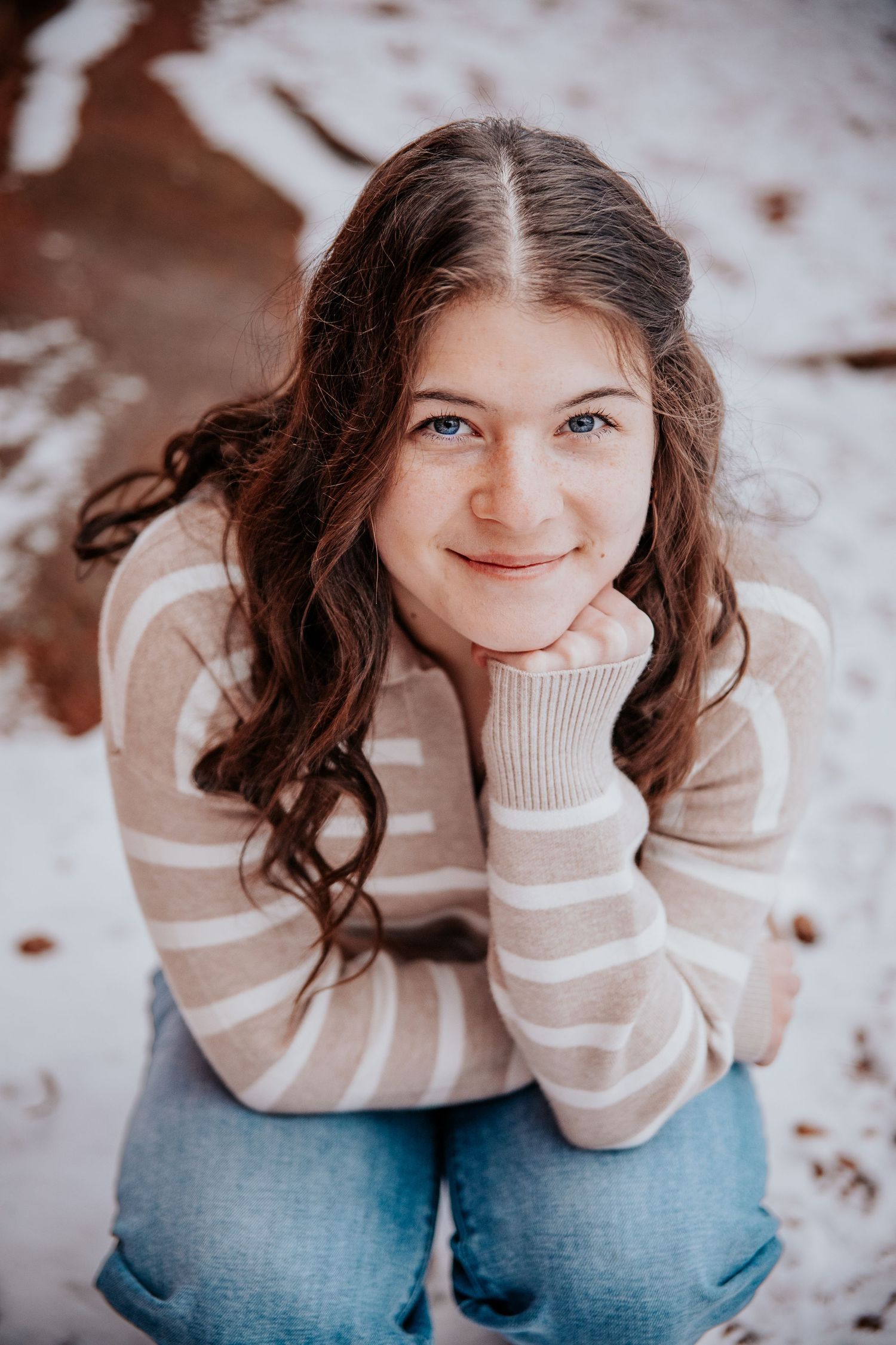 Winter portrait series featuring striped sweater against snowy backdrop.