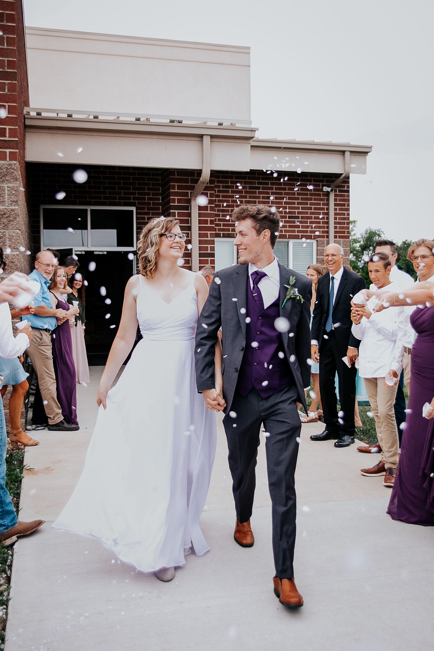 Newlyweds exit their wedding ceremony while guests shower them with bubbles.