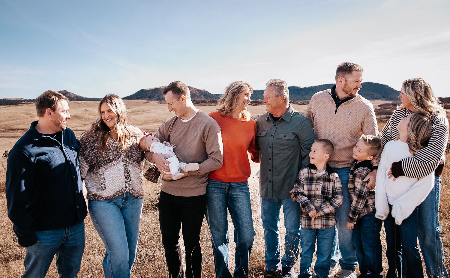 A group of people stand together in a line against a scenic mountain backdrop during sunset.