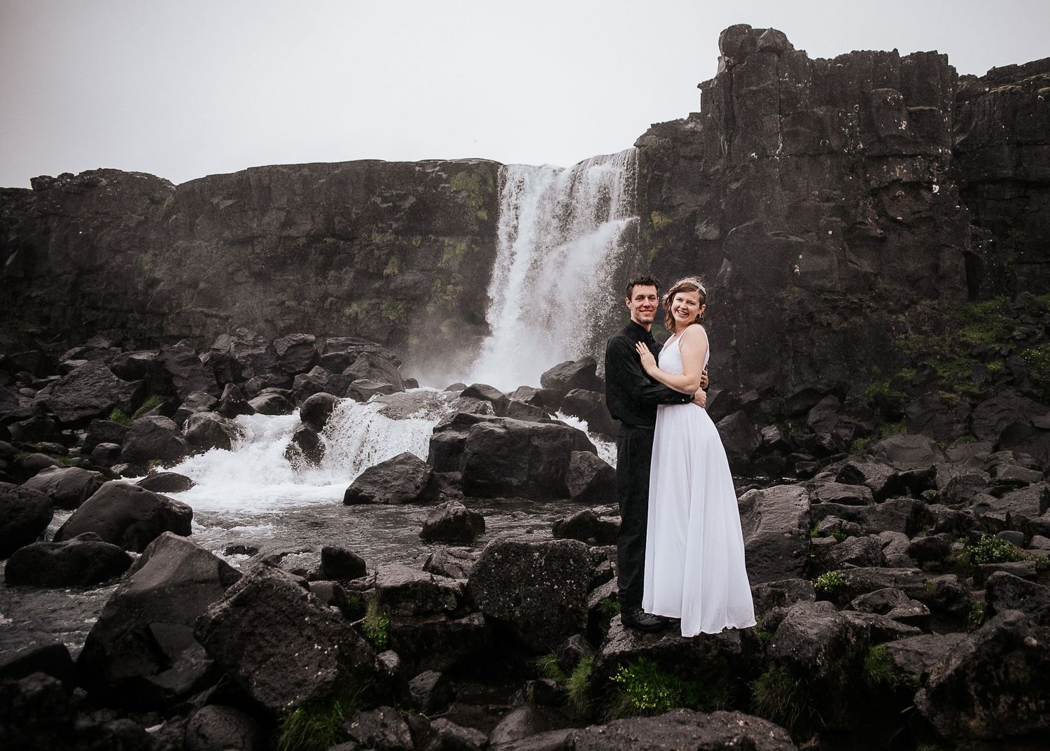 A couple poses for a wedding portrait in front of a majestic waterfall.