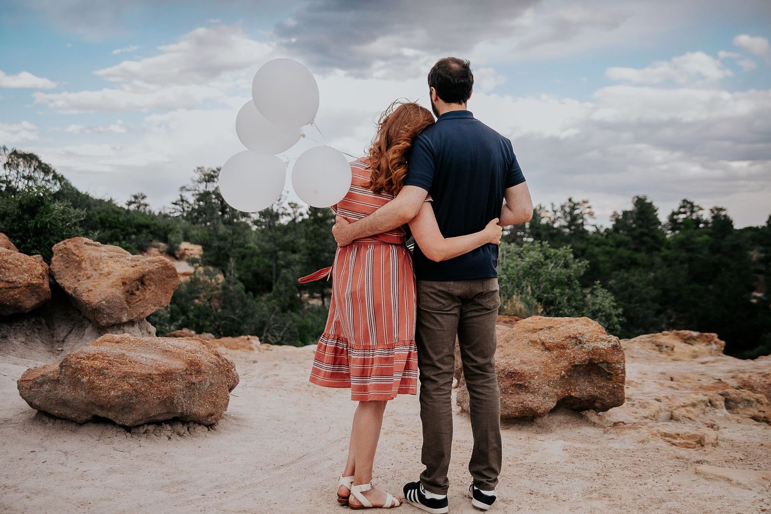 Two people embracing while sitting on red rocks with mountain views.