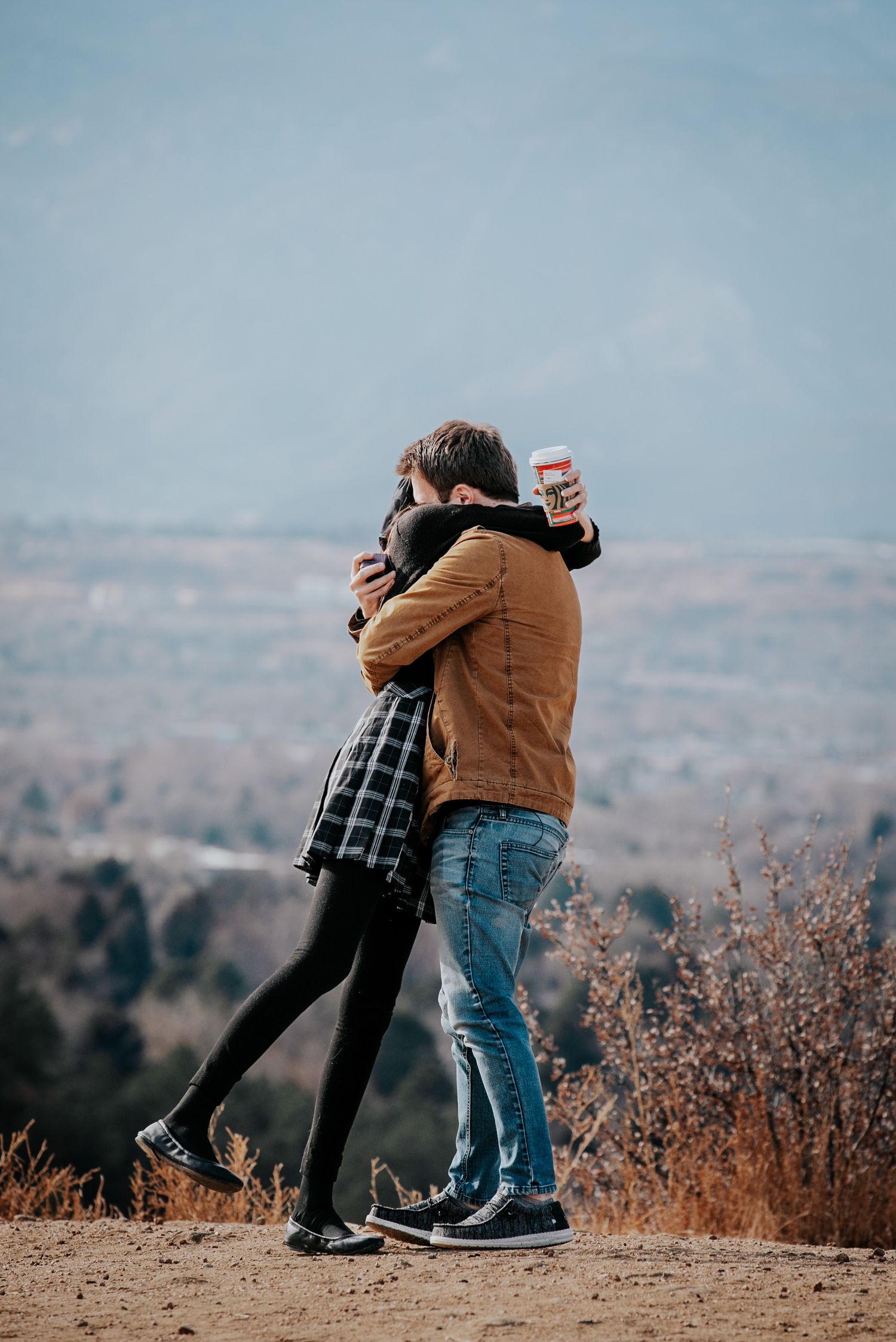 Happy couple embraces on mountain overlook after romantic proposal.