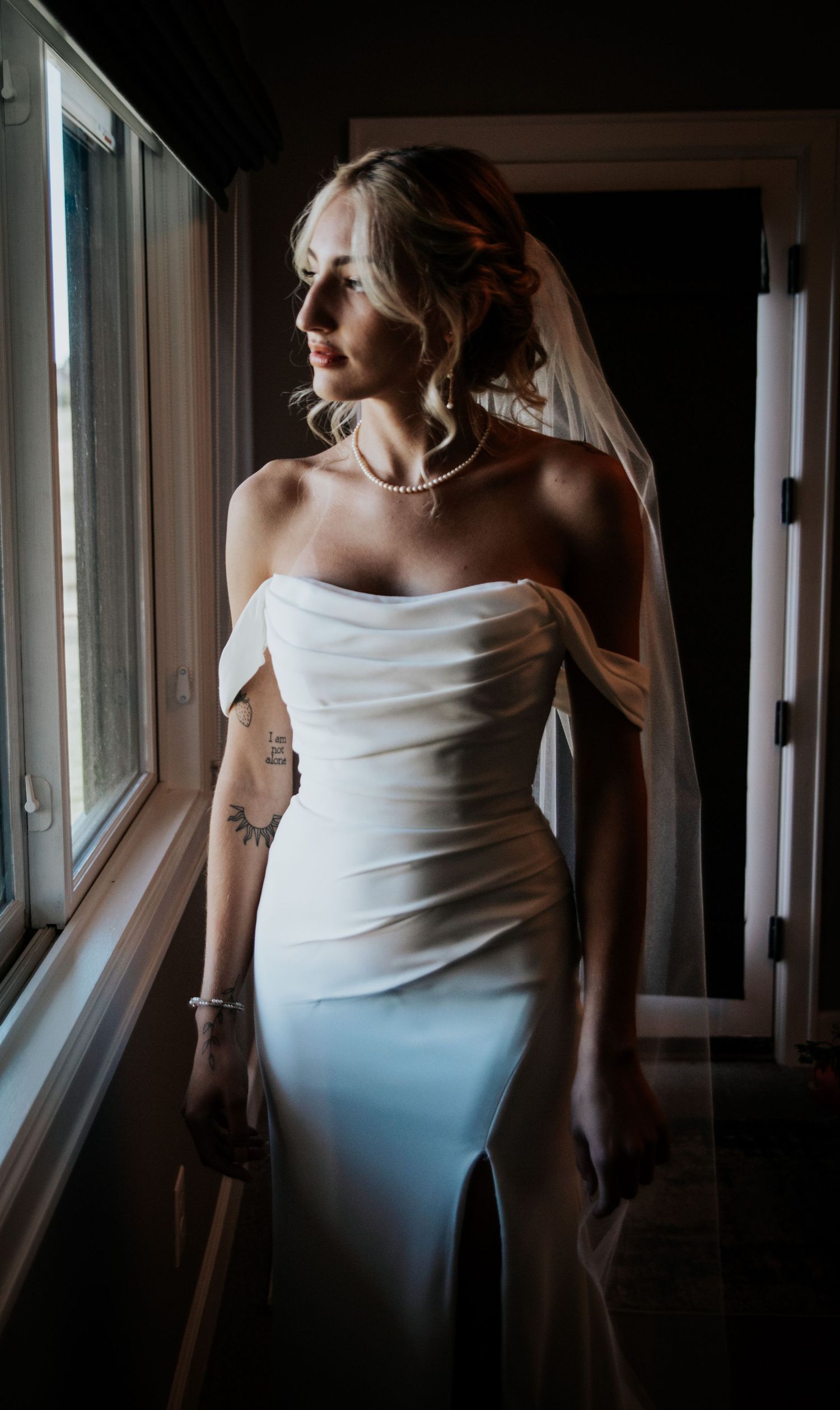 Dramatic window light portrait of bride in strapless white gown.