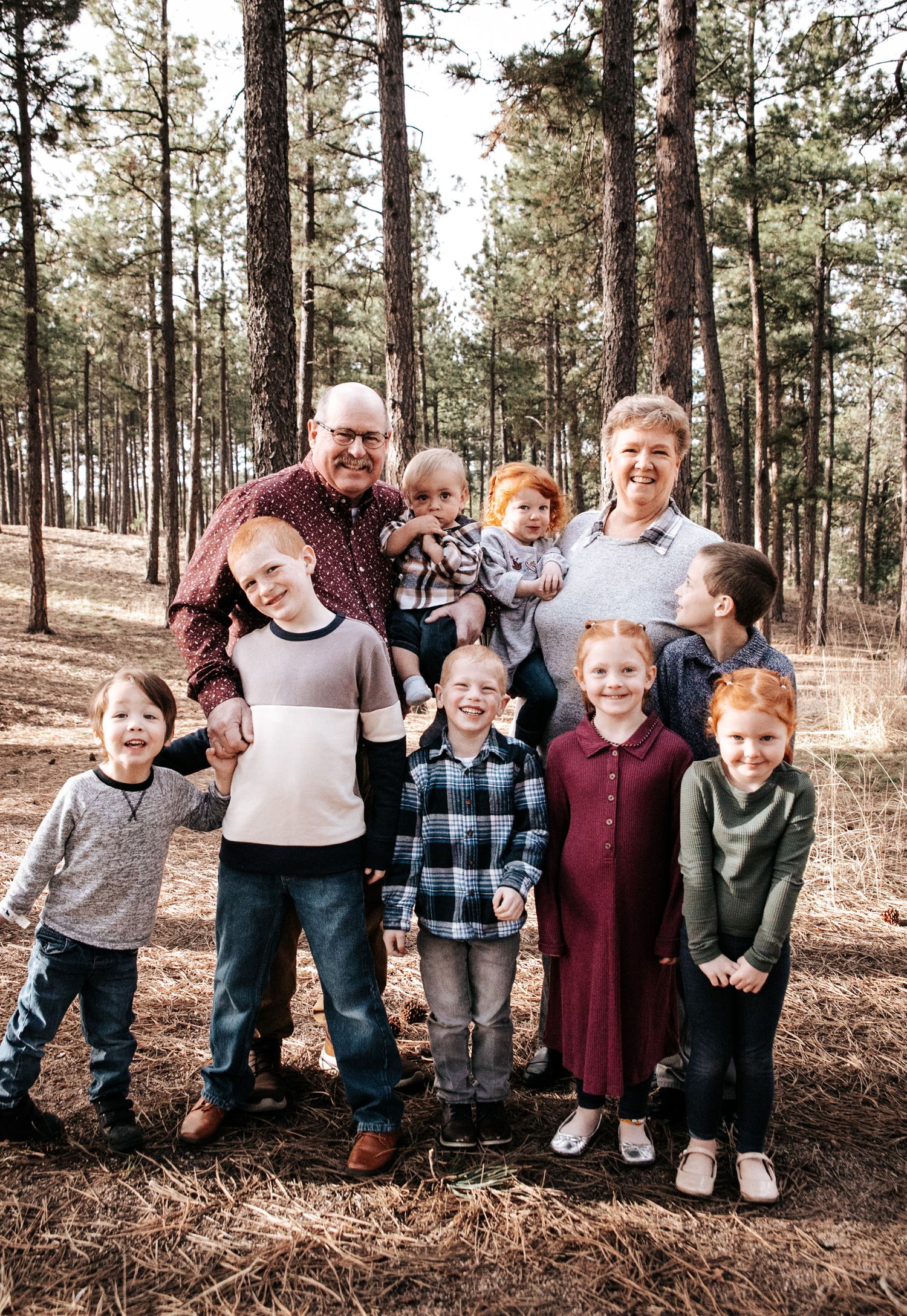 Multi-generational family portrait in a wooded pine forest setting.