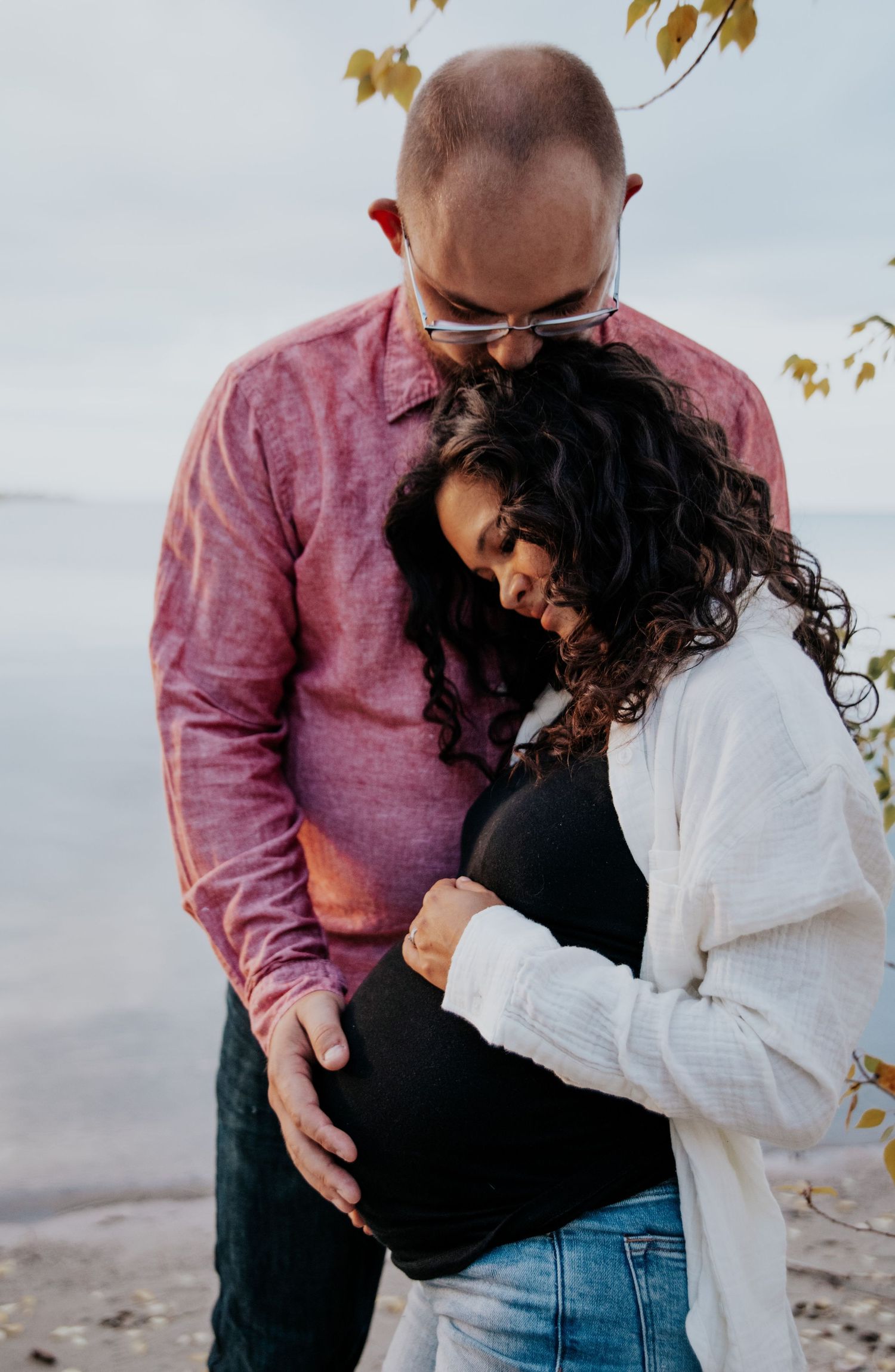 A couple shares an intimate moment on a beach with autumn leaves in the foreground.