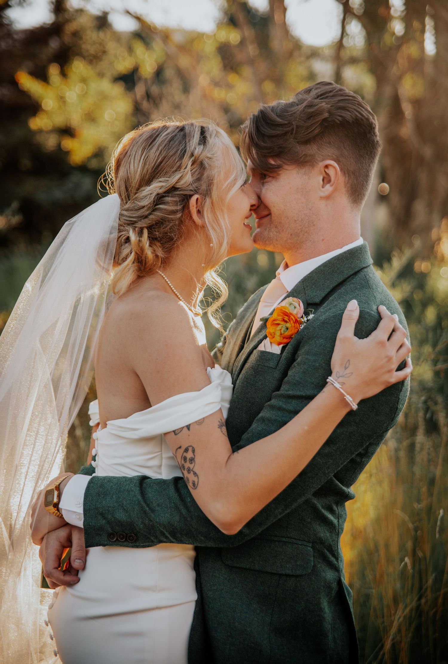 Emotional wedding embrace in golden light with white dress and dark green suit.