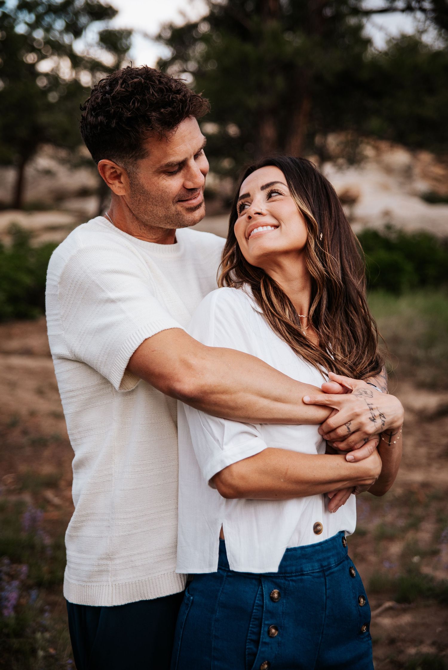 Couple in white shirts embrace and share loving glances against a nature backdrop at Ute Valley Park in Colorado Springs