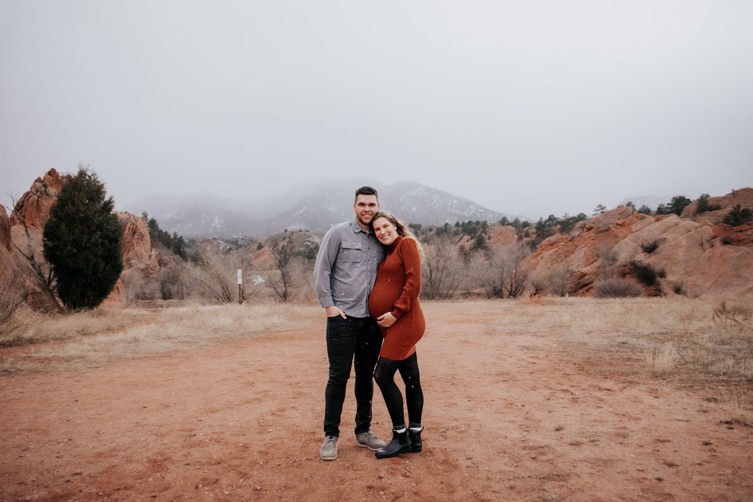 Two people embrace in a romantic photoshoot against red rock formations and a serene lake backdrop.
