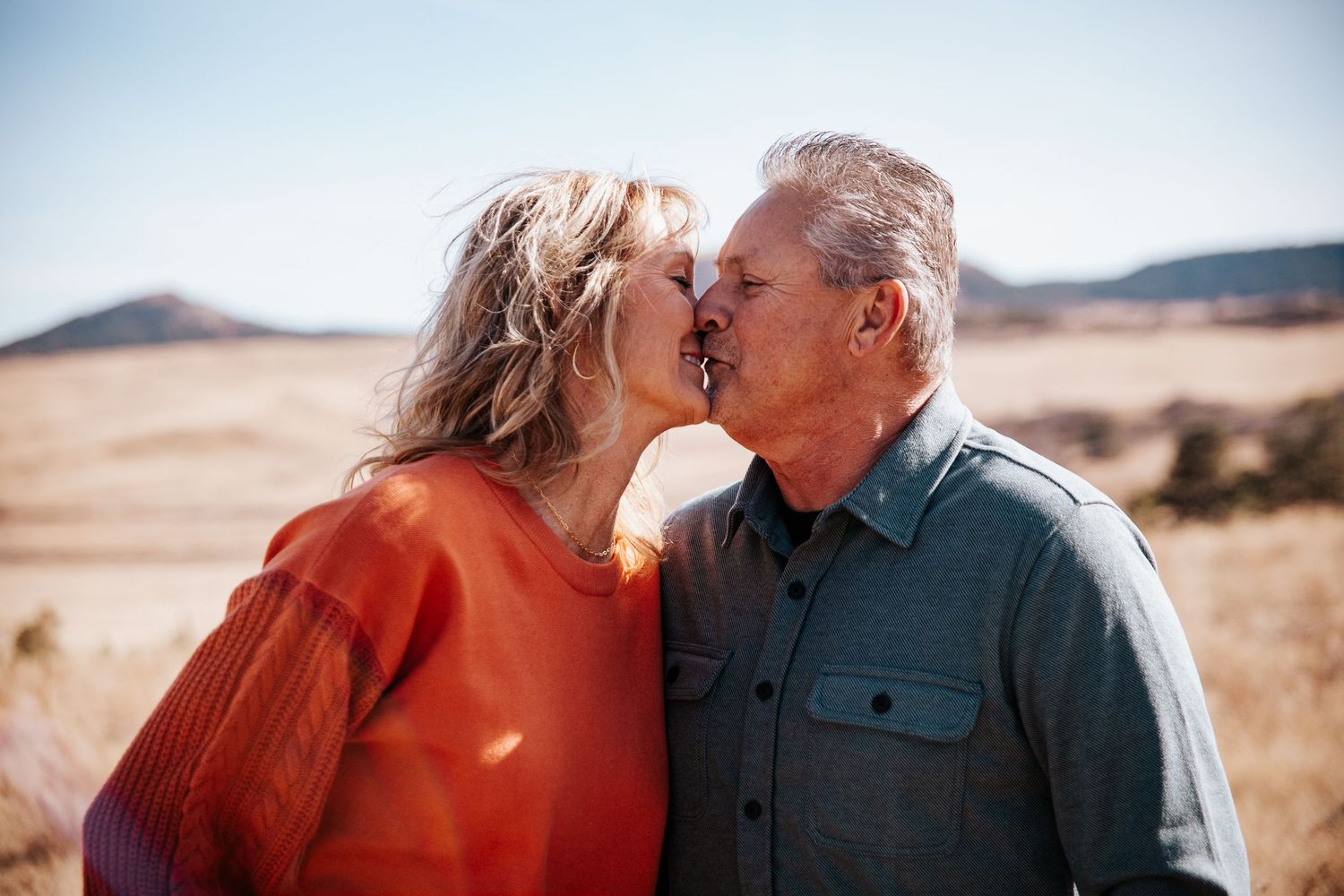 Couple sharing an intimate moment outdoors with mountains visible in the background.