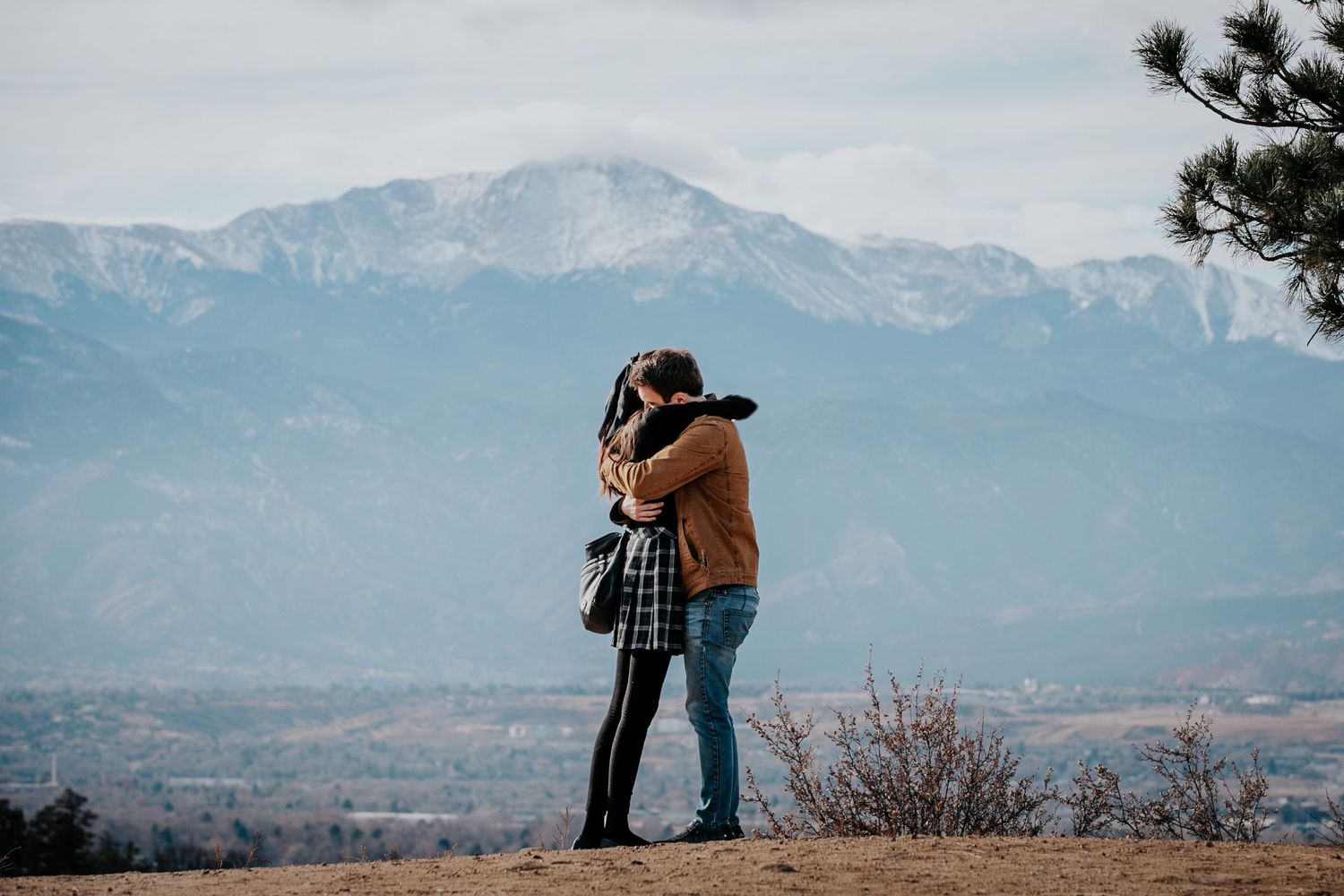 Pair shares intimate moment against backdrop of majestic snow-capped mountains.
