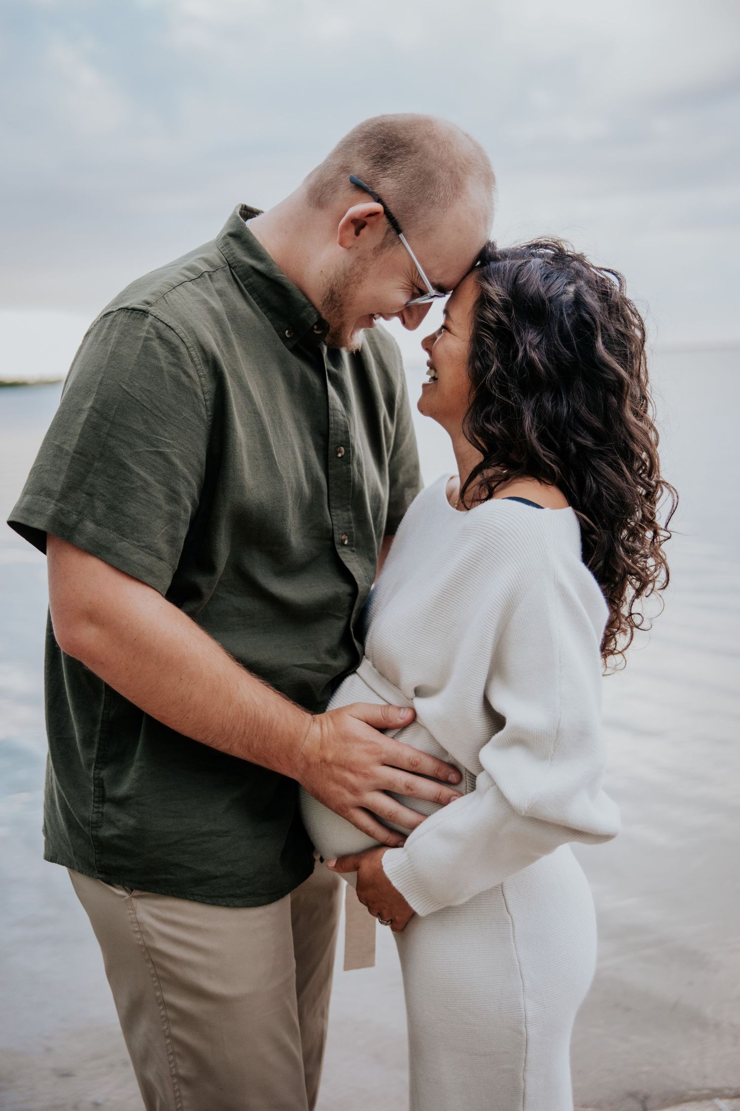 Beachside maternity photoshoot with couple in casual attire.