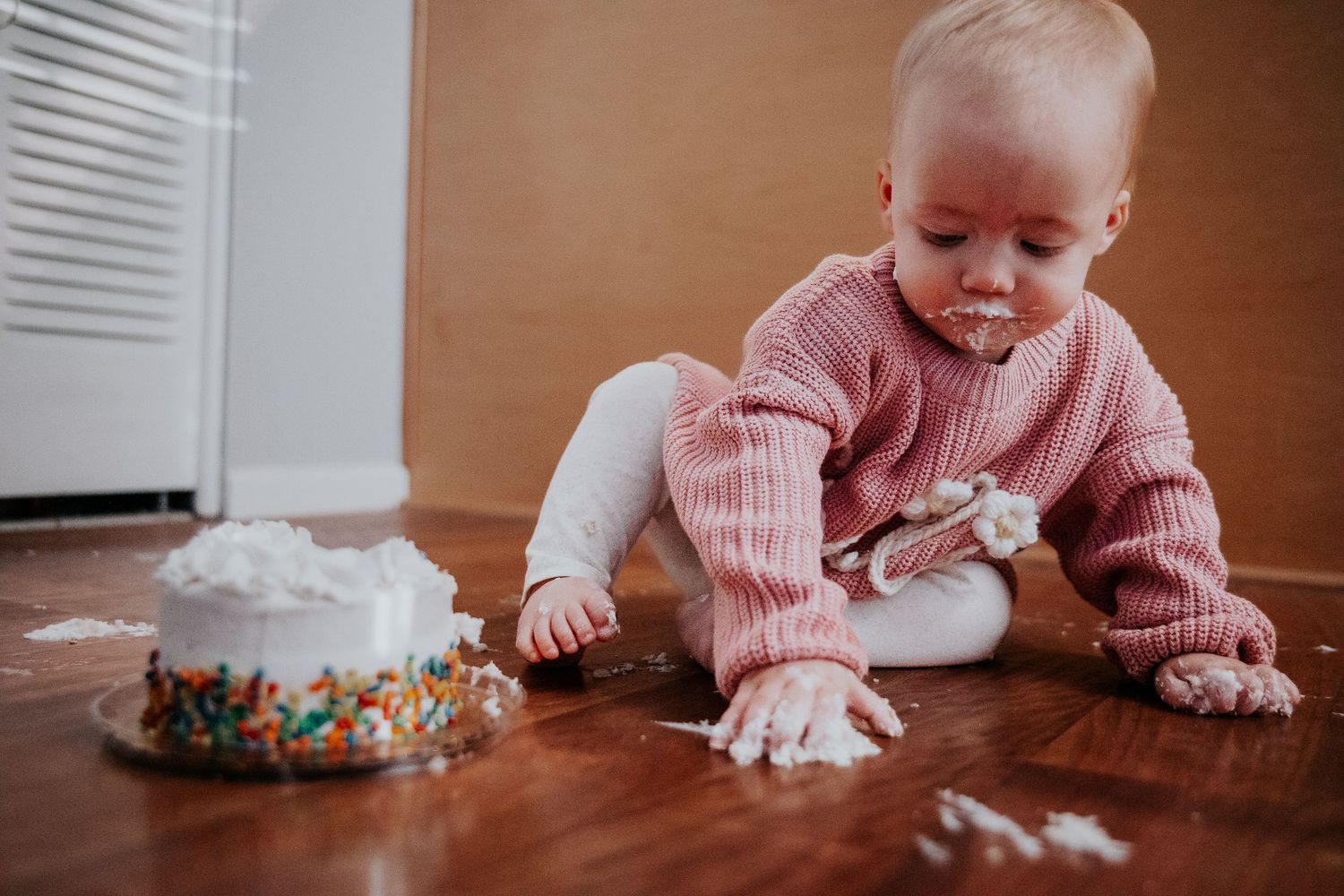 A cake smash photo showing a decorated smash cake and scattered frosting on wooden floor.