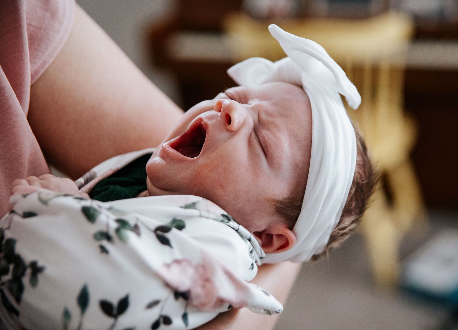 Close-up of sleeping newborn wearing floral print outfit and white bow headband.