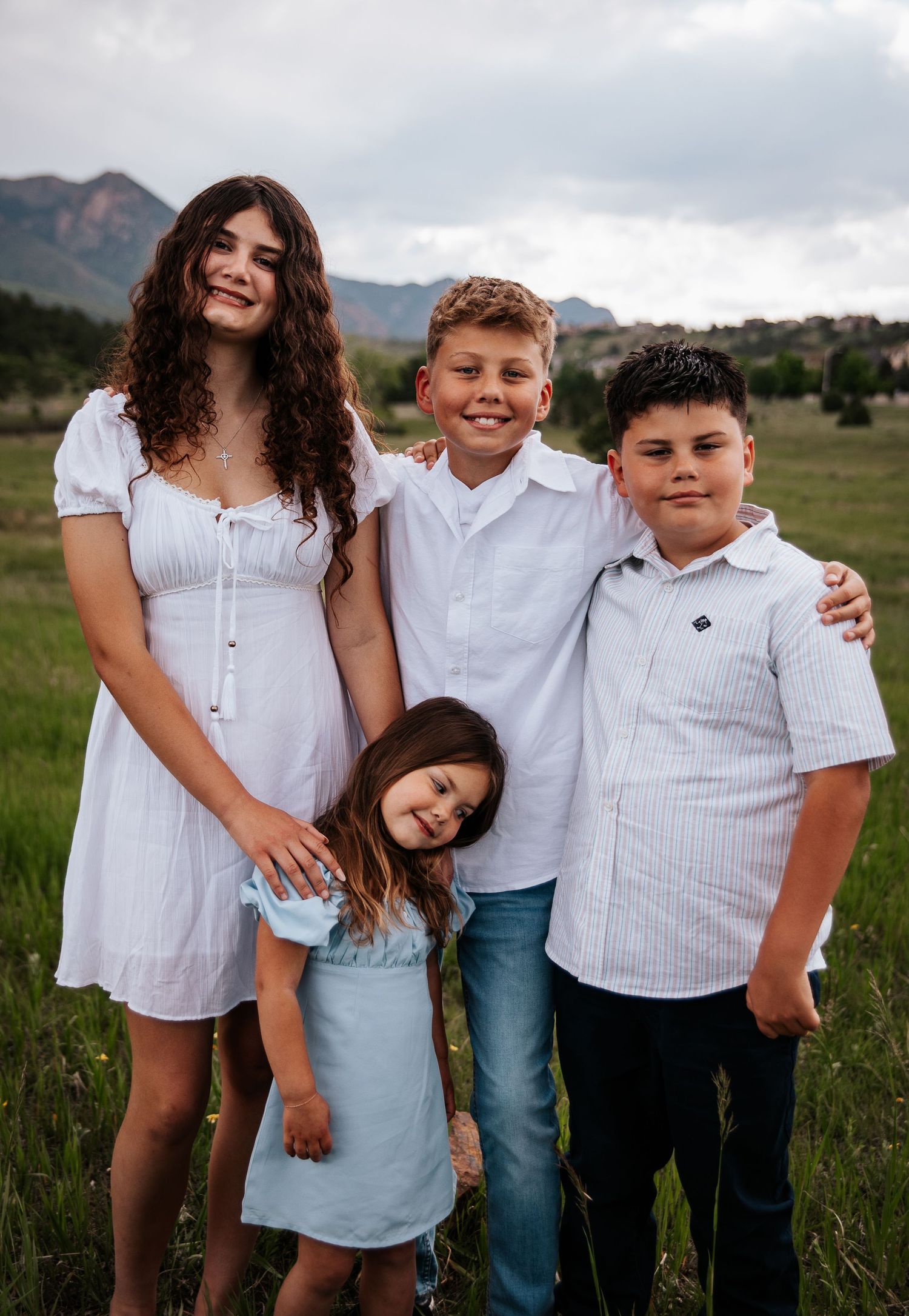 A group wearing coordinated white outfits poses casually in a mountain meadow at Ute Valley Park in Colorado Springs