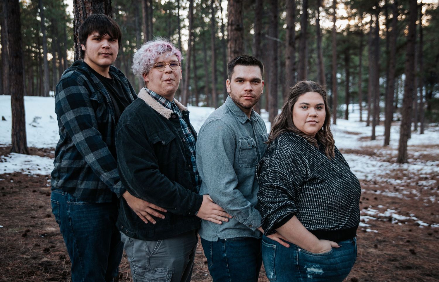 Family portrait of four people standing together in winter forest setting.