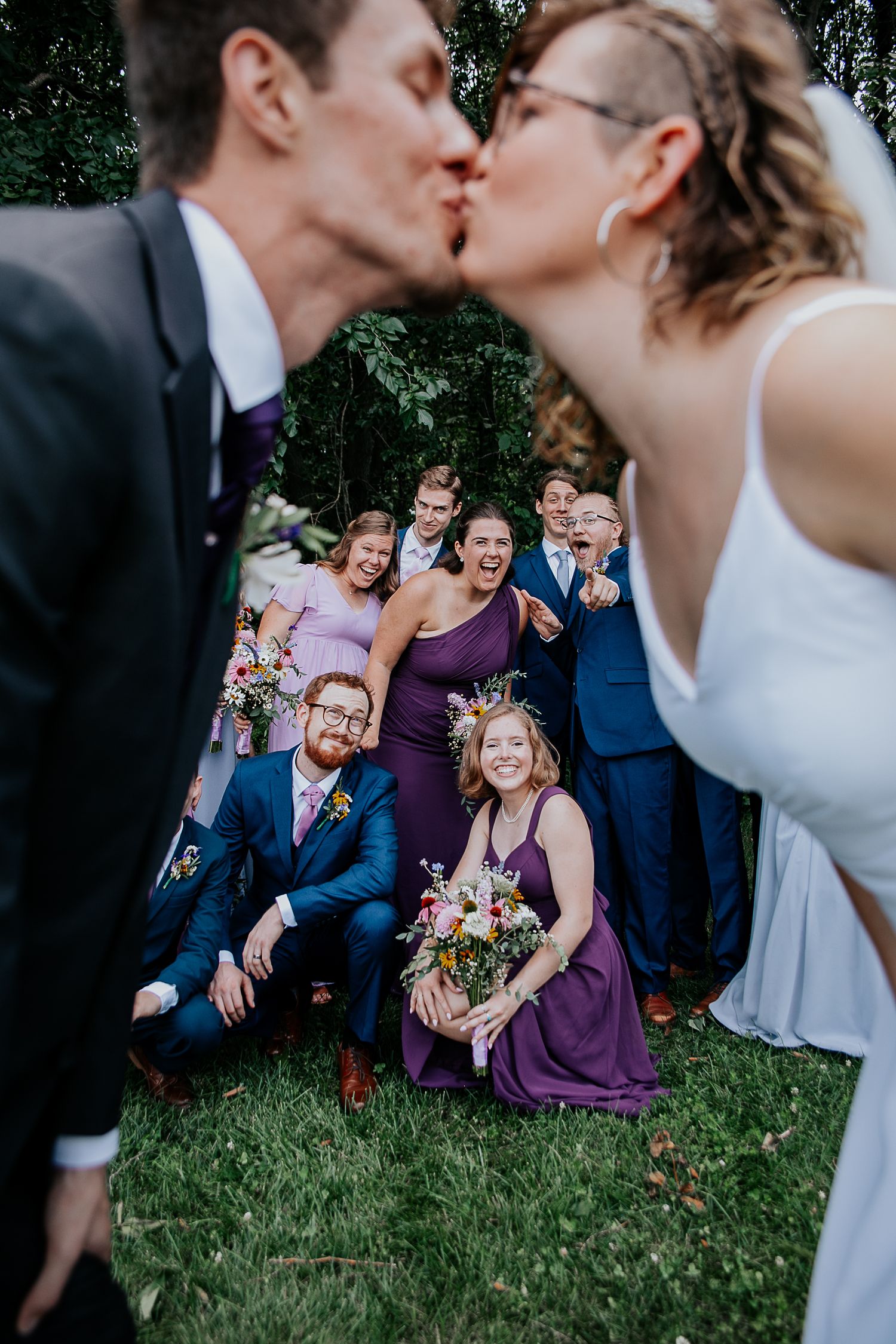 Wedding celebration in outdoor garden setting with bridal party in purple and navy attire.