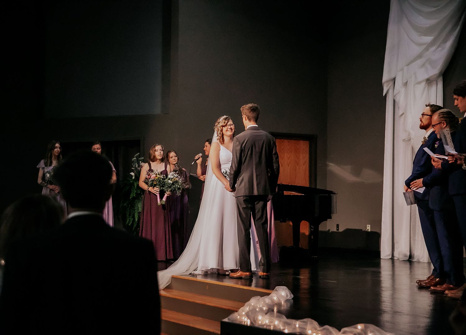 Wedding couple exits church ceremony down aisle decorated with white fabric and greenery.