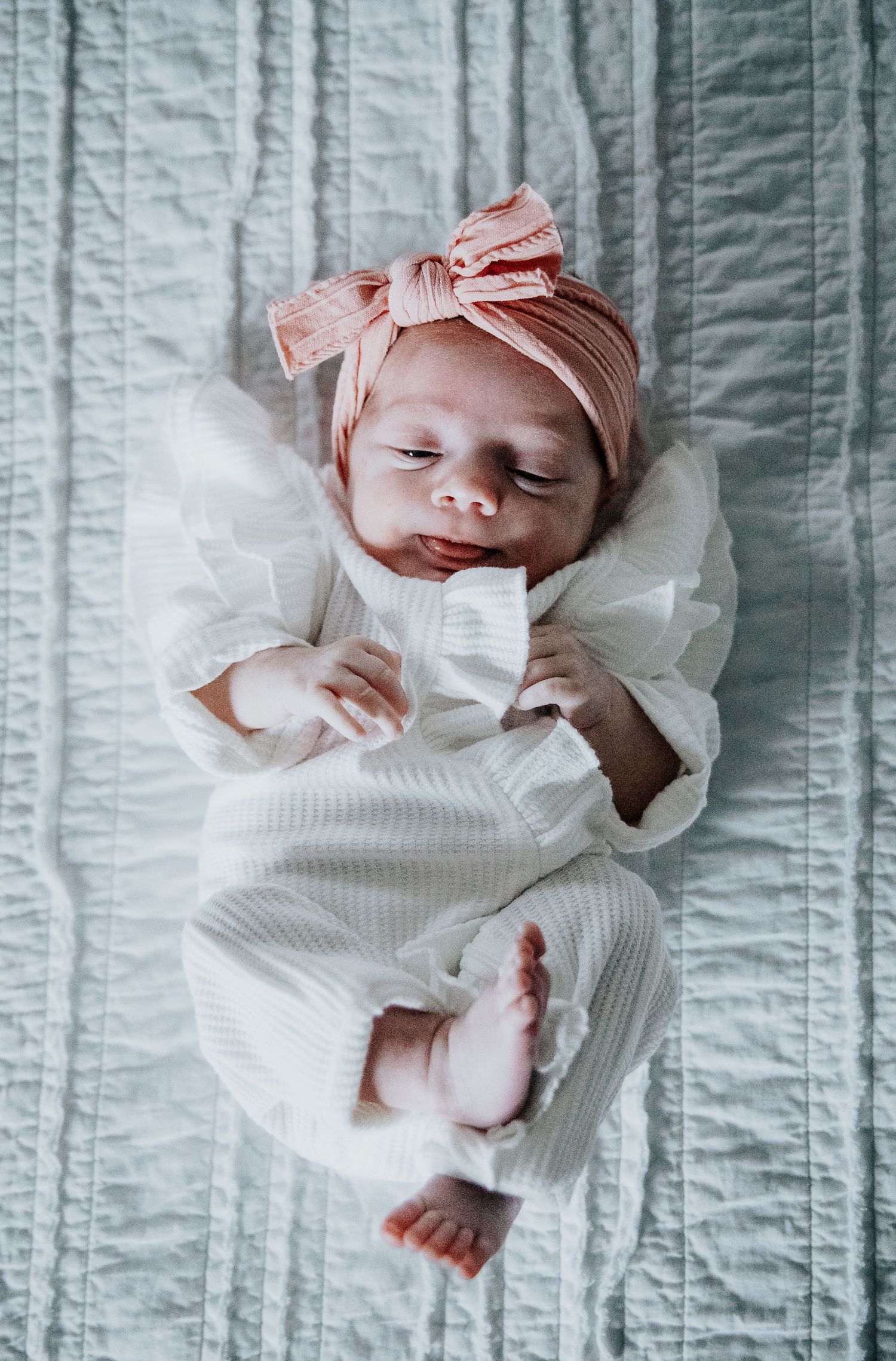 Newborn baby in white clothing lying on striped fabric showing progression of sleeping positions.