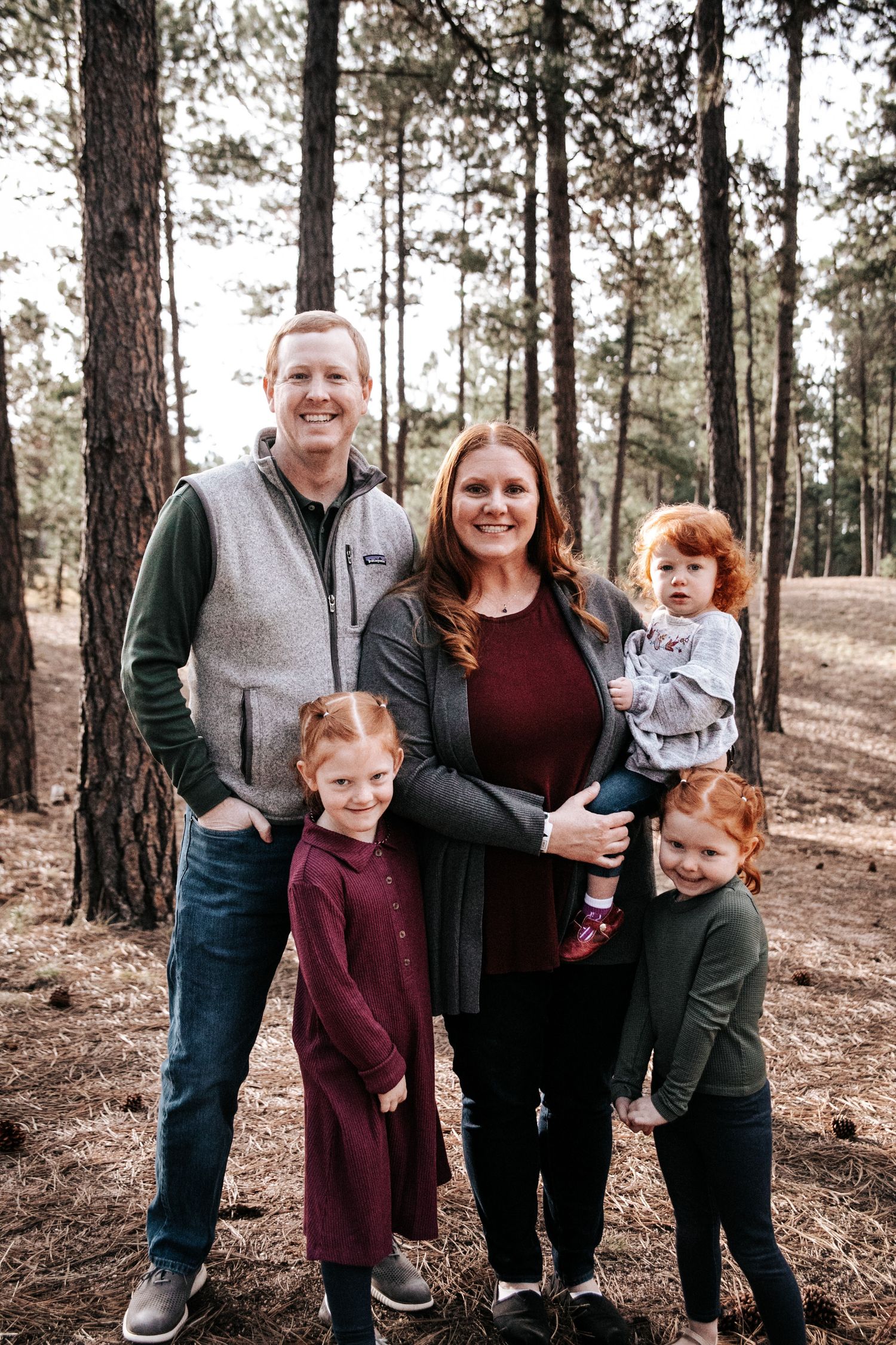 Family of five smiling together in a pine forest setting.