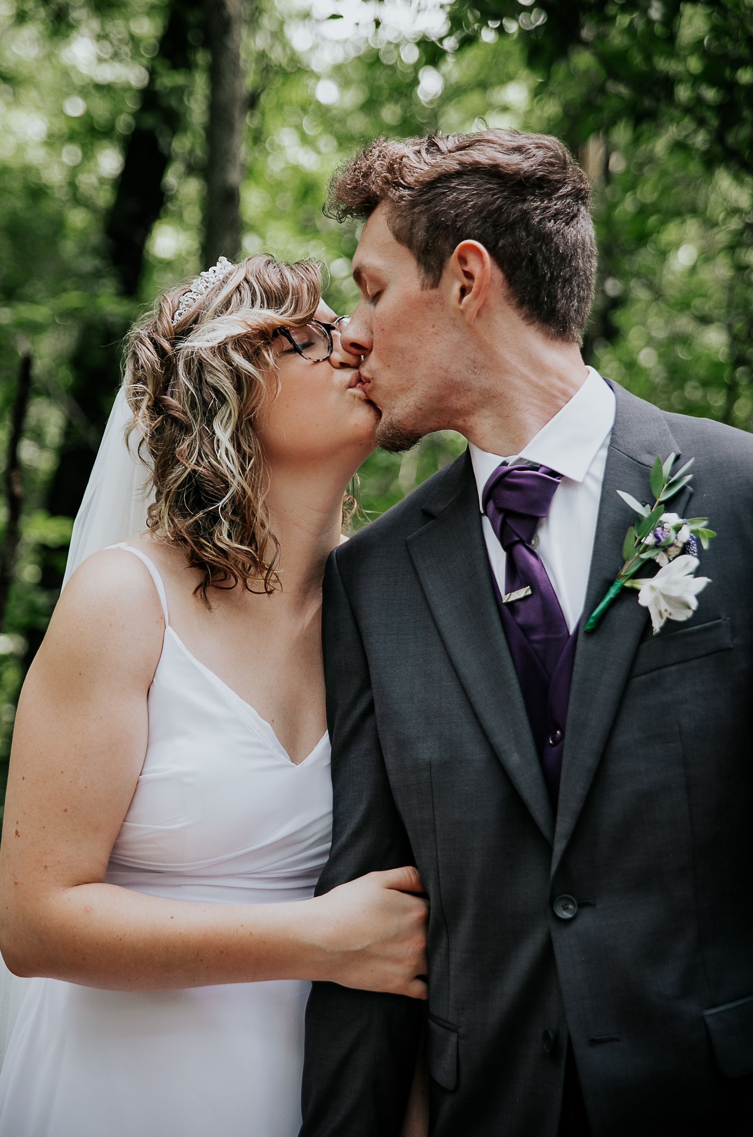 Wedding couple shares intimate kiss in forest setting.
