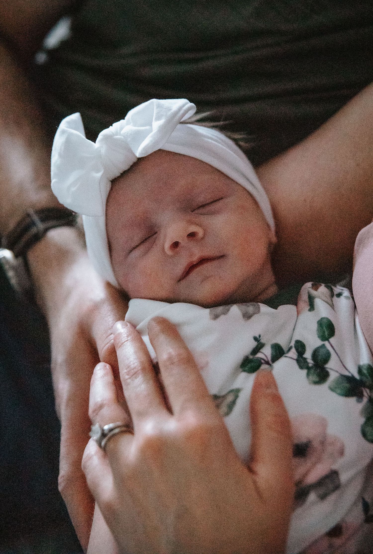 Close-up shots of a sleeping newborn wrapped in a white swaddle with delicate green leaf details.