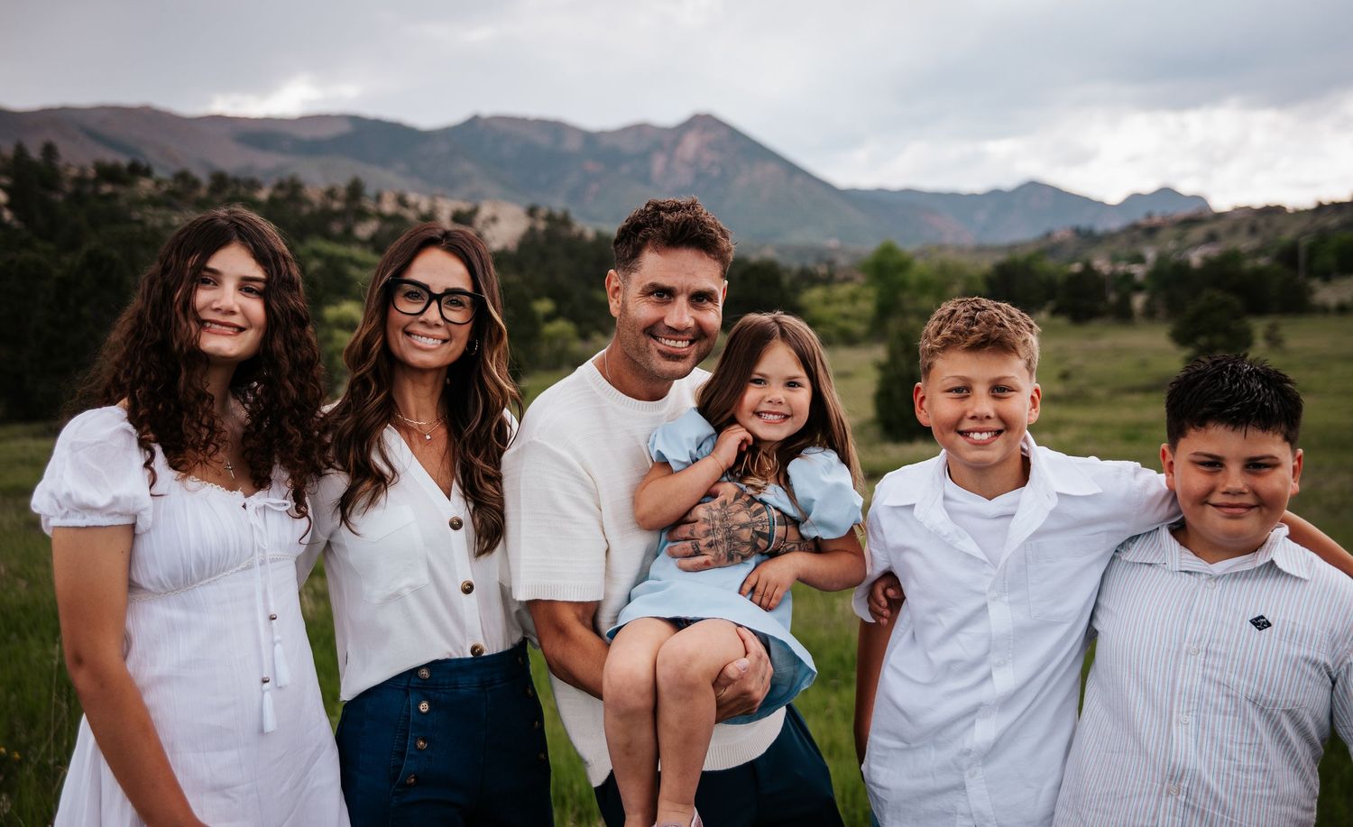 Family portrait of people wearing white and blue outfits against mountain backdrop at Ute Valley Park in Colorado Springs