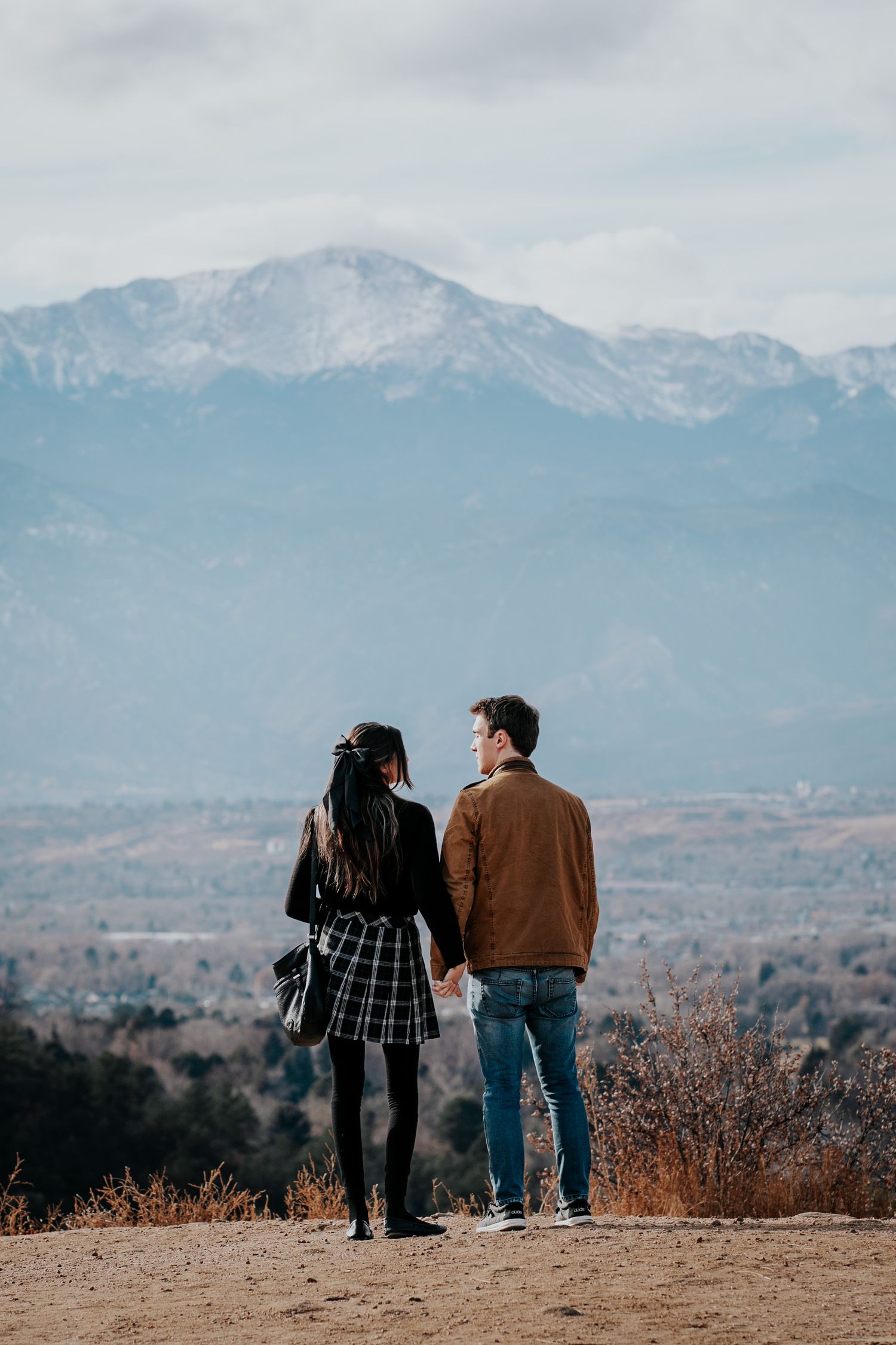 Couple stands together overlooking mountain vista on a cloudy day with dramatic landscape in background.