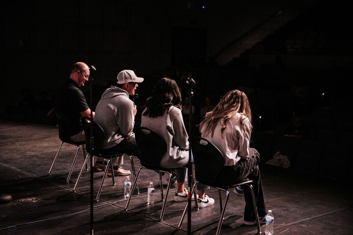 Group of people seated in chairs on a dark stage during a presentation or discussion.