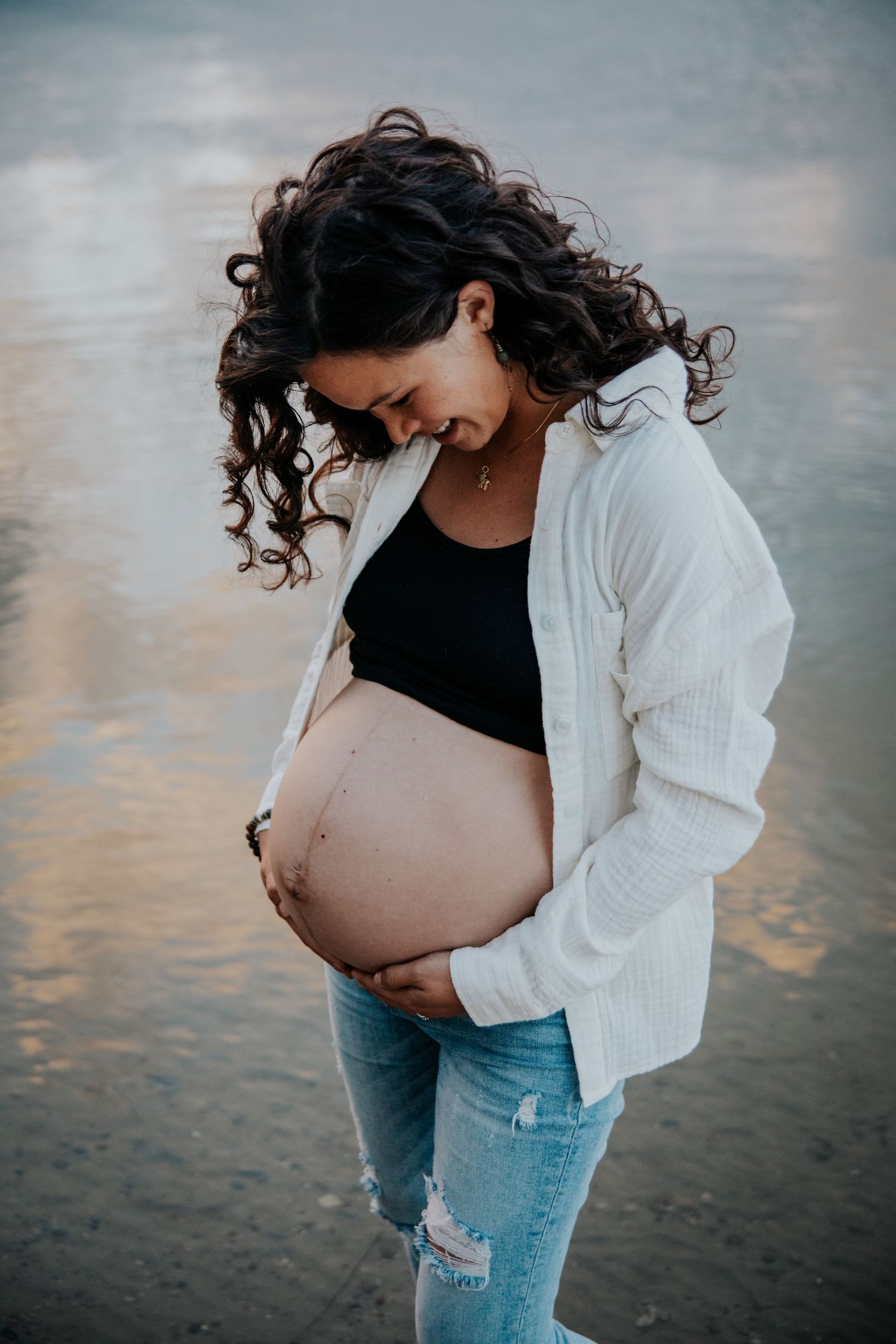 Maternity photos taken at the beach during golden hour showing a pregnant woman in casual attire.
