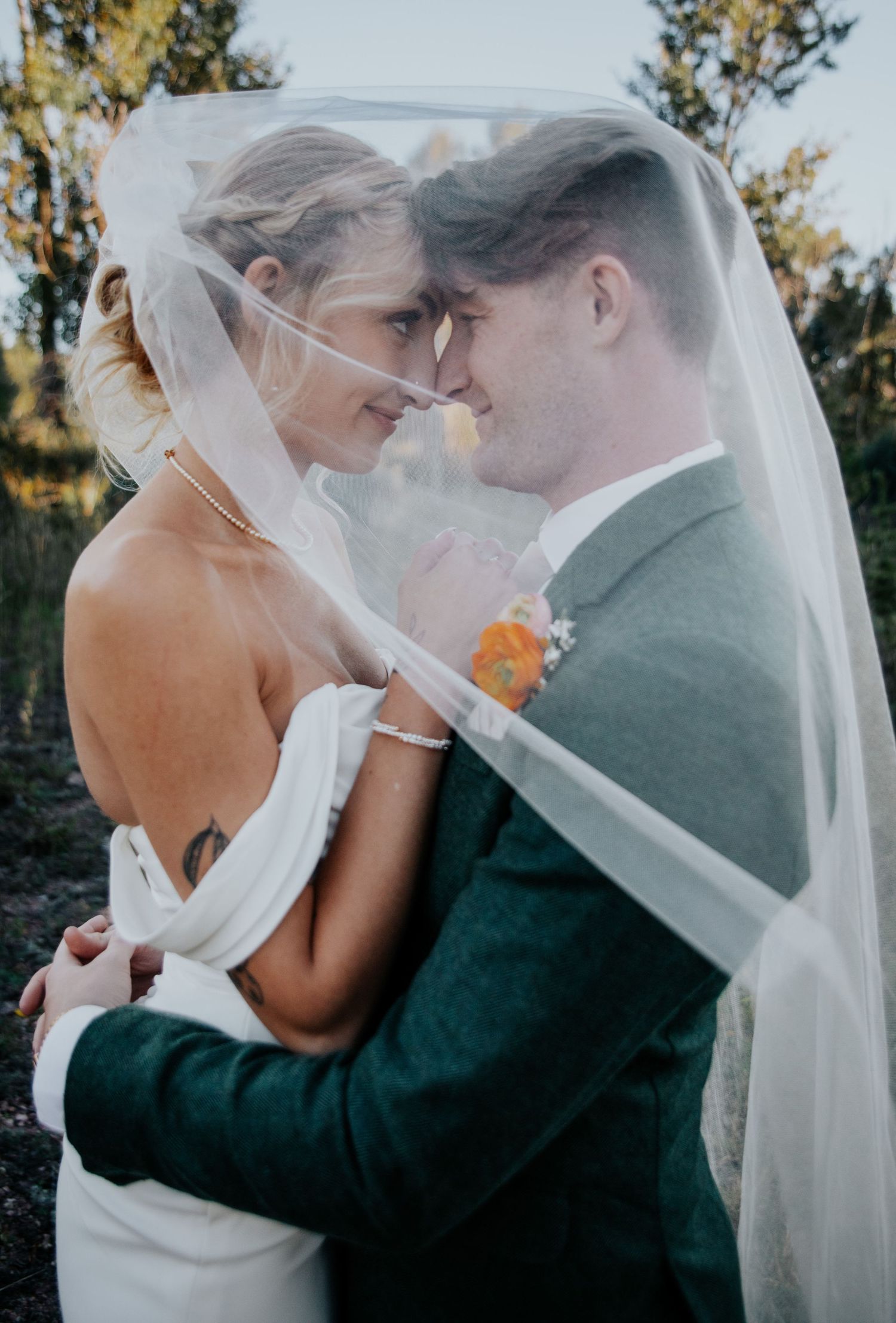 Romantic embrace under flowing white veil in natural outdoor setting.