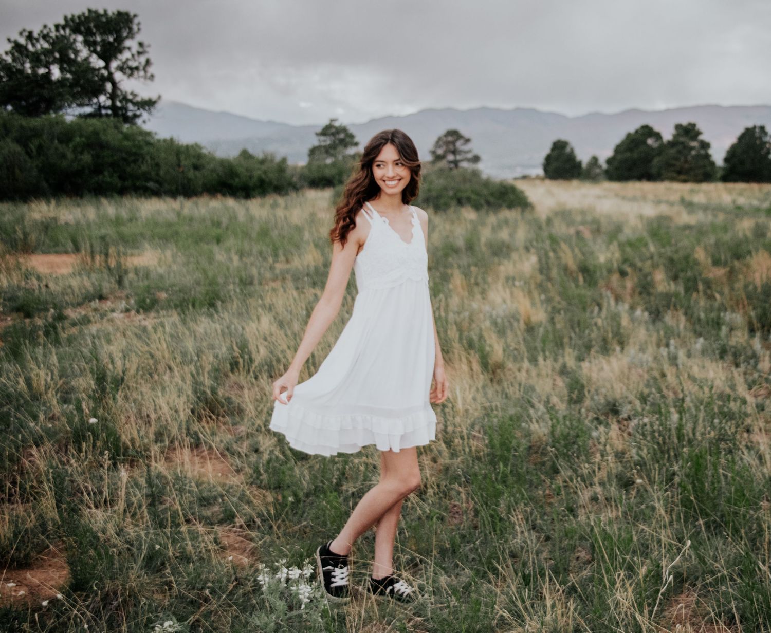 A figure in a flowing white dress twirls gracefully in a field with mountains in the distant background.
