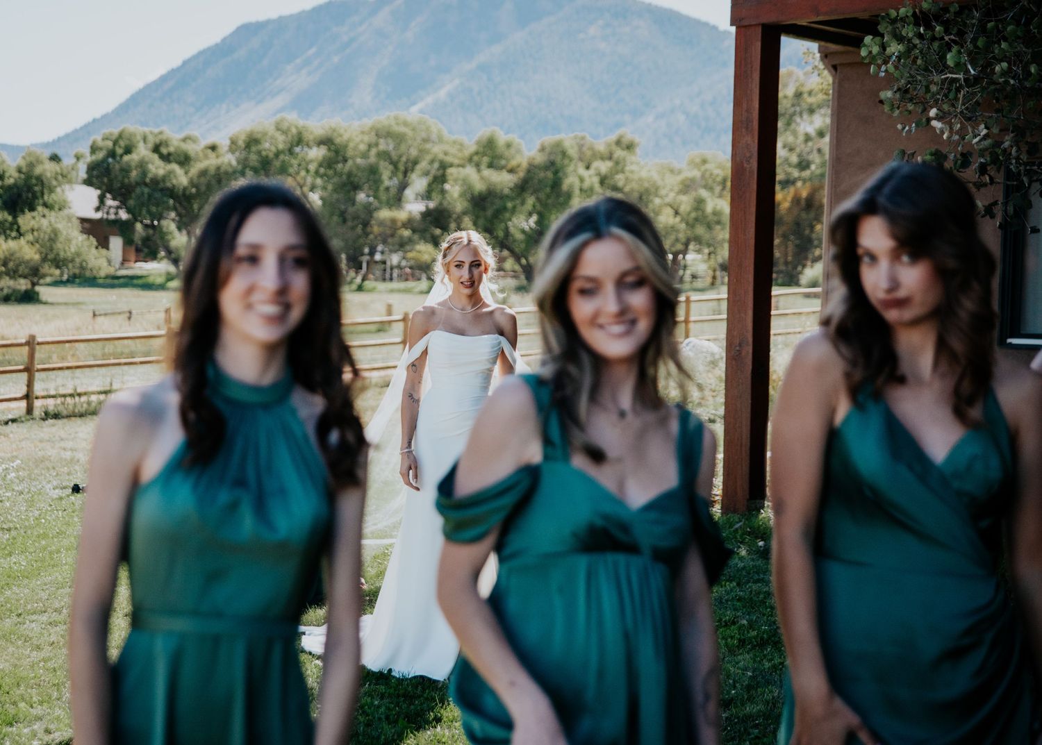 Wedding party in emerald dresses outdoors with mountain backdrop.