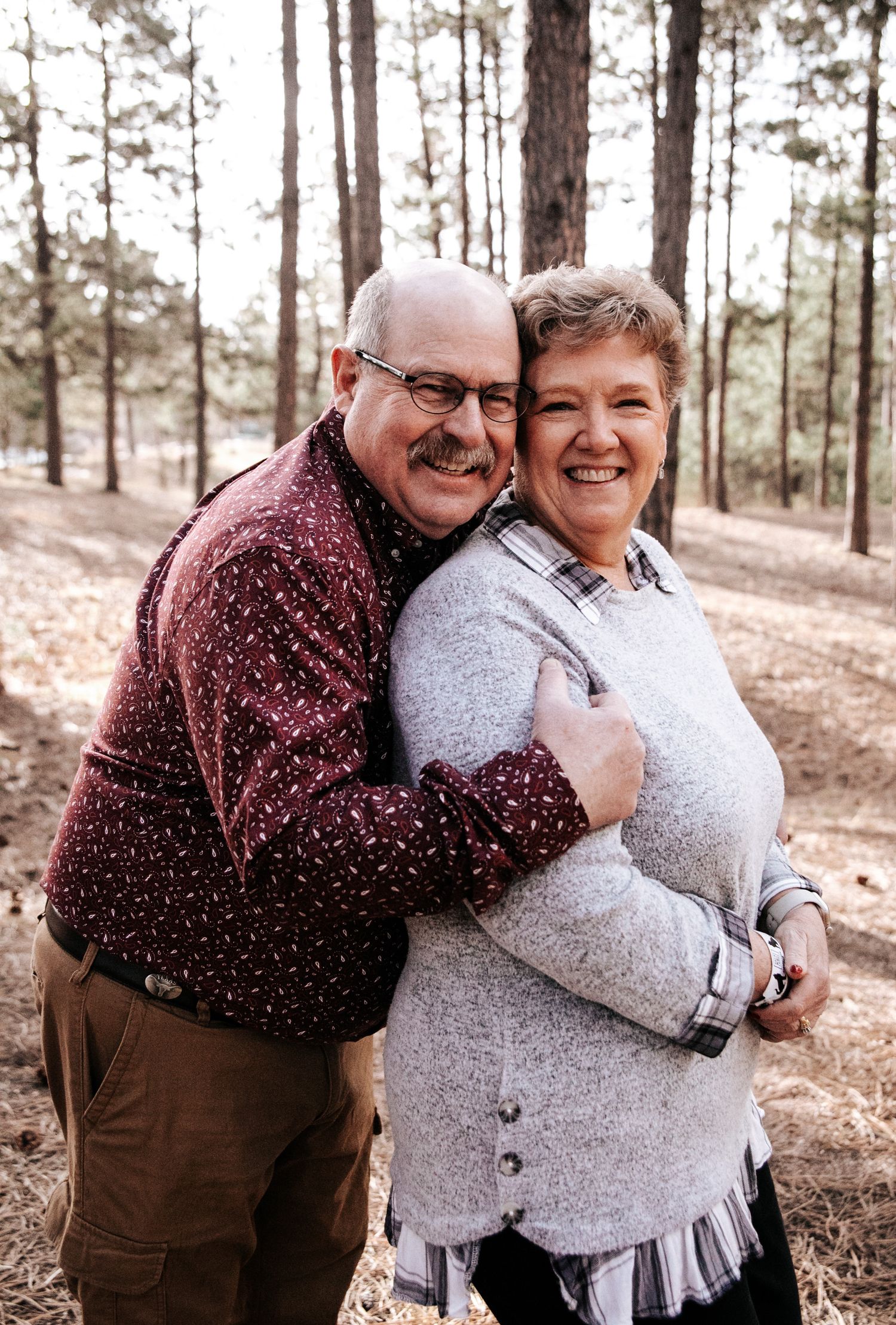 Couple sharing a joyful embrace in a pine forest setting.