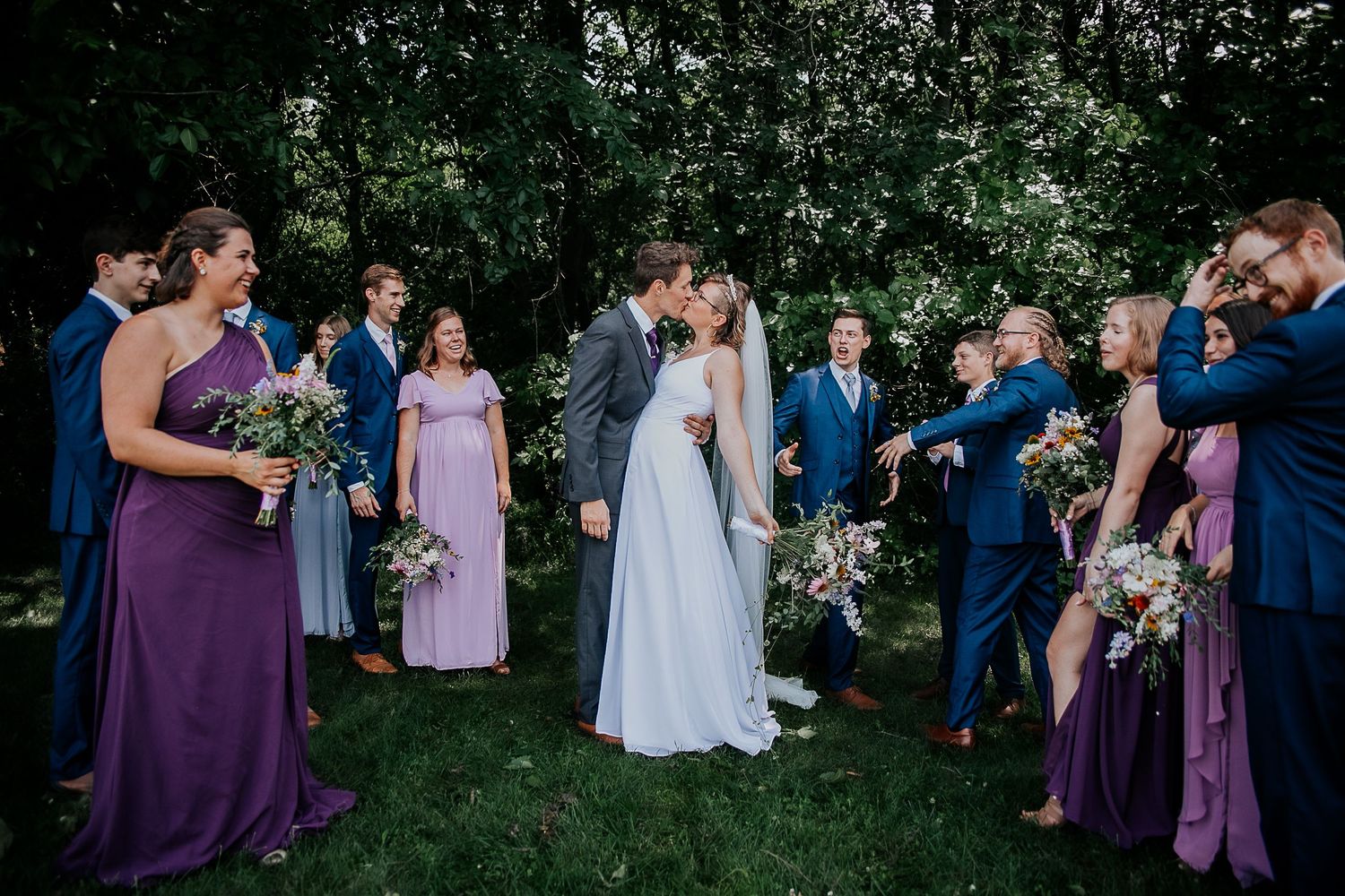 Fun bridal party photo with attendants gathered around groom sitting on ground.