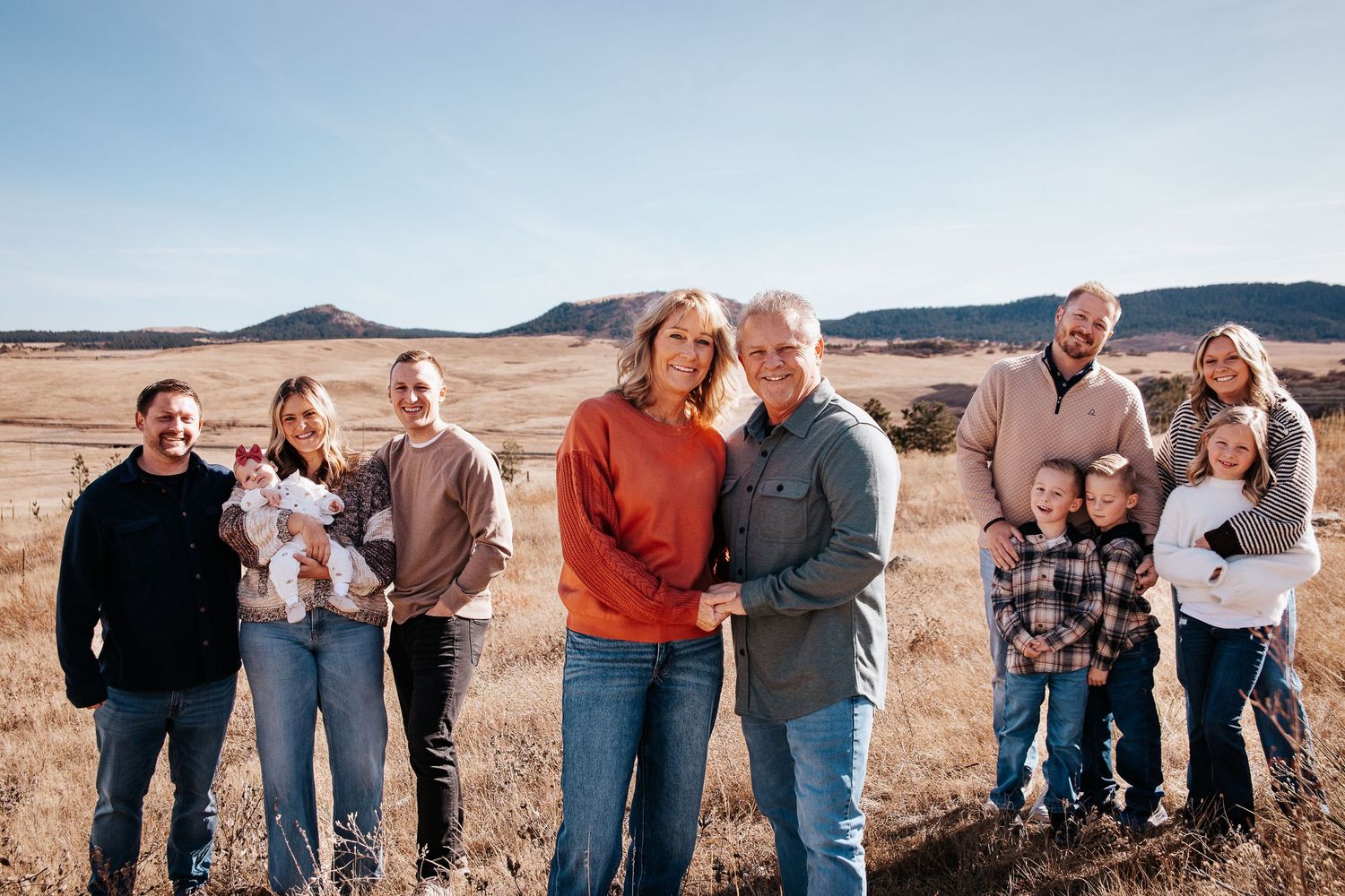 Group of people laughing and embracing outdoors against a desert mountain landscape in casual clothing.